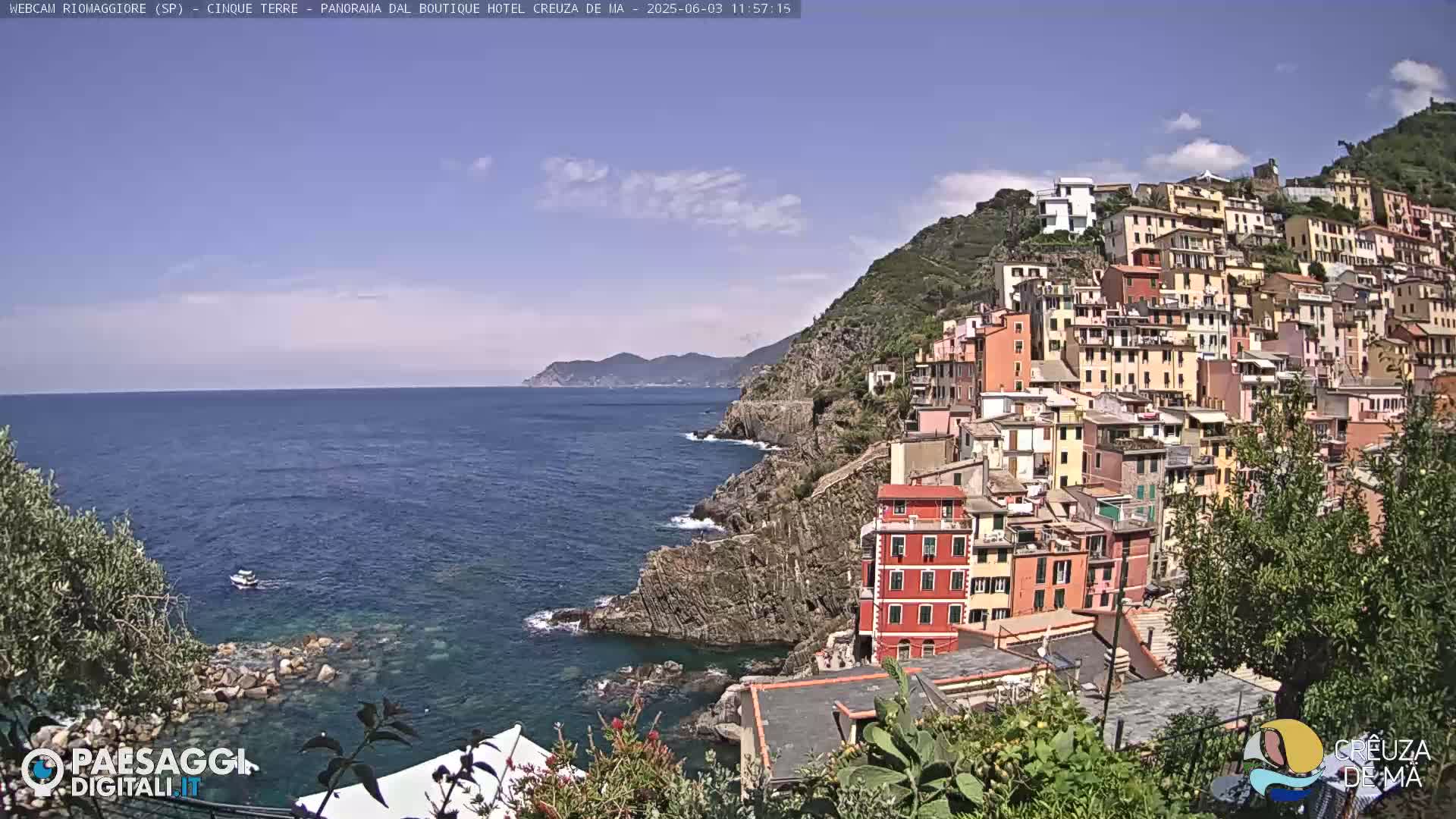 A colorful village clings to a steep hillside overlooking a calm blue sea on a sunny day.