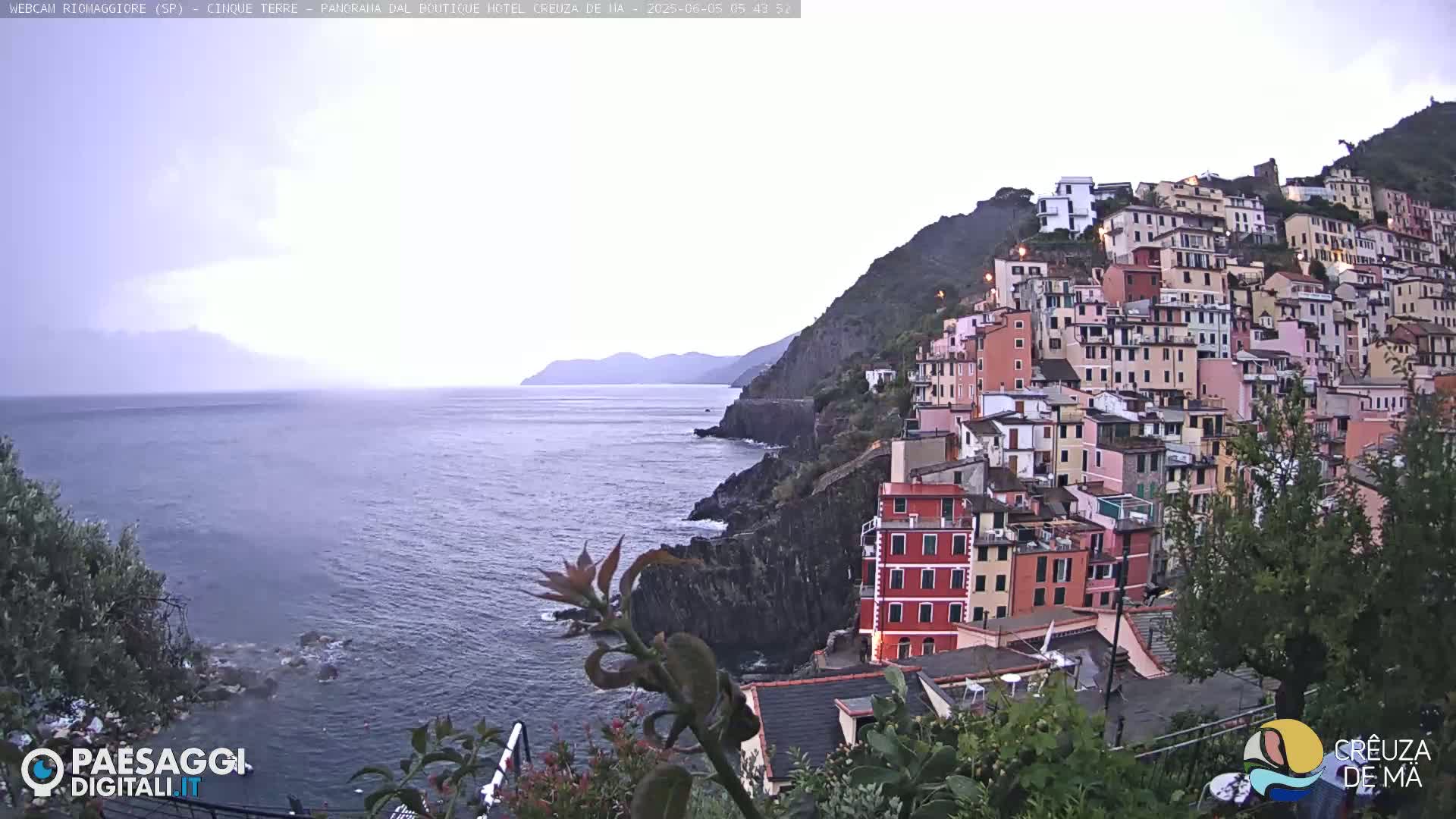 A colorful hillside village overlooks a calm sea under an overcast sky.
