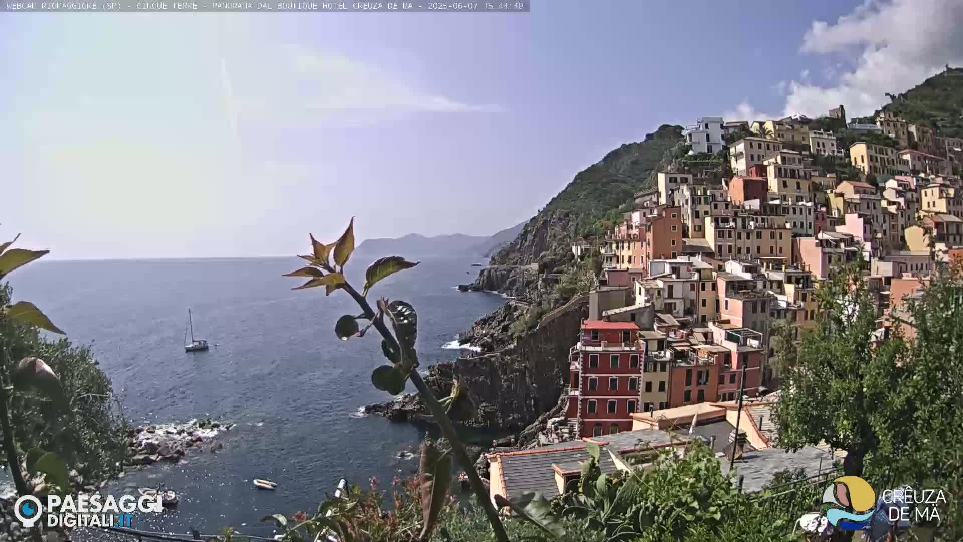A colorful village clings to a steep hillside overlooking a calm blue sea on a sunny day.