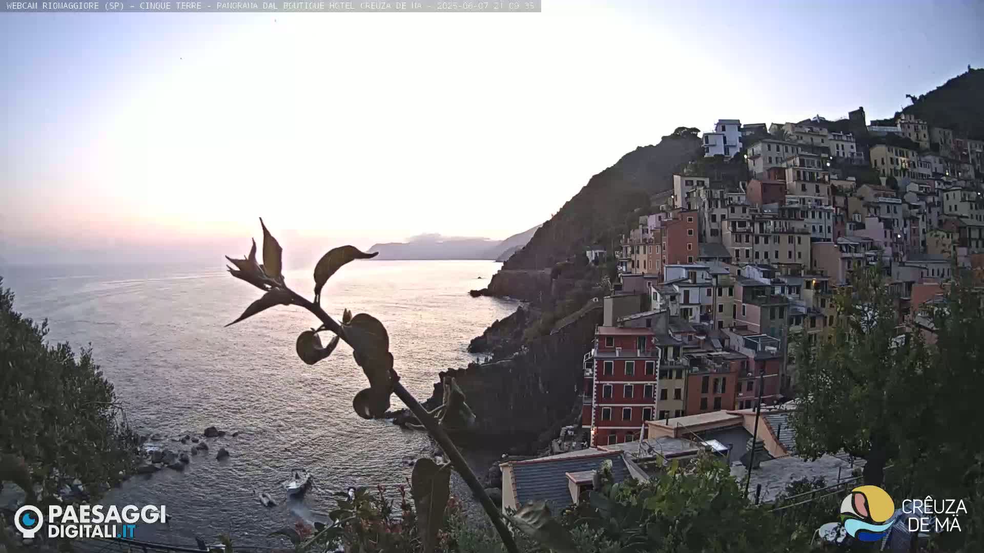 A coastal village of colorful buildings clings to a steep hillside overlooking a calm sea under a twilight sky.