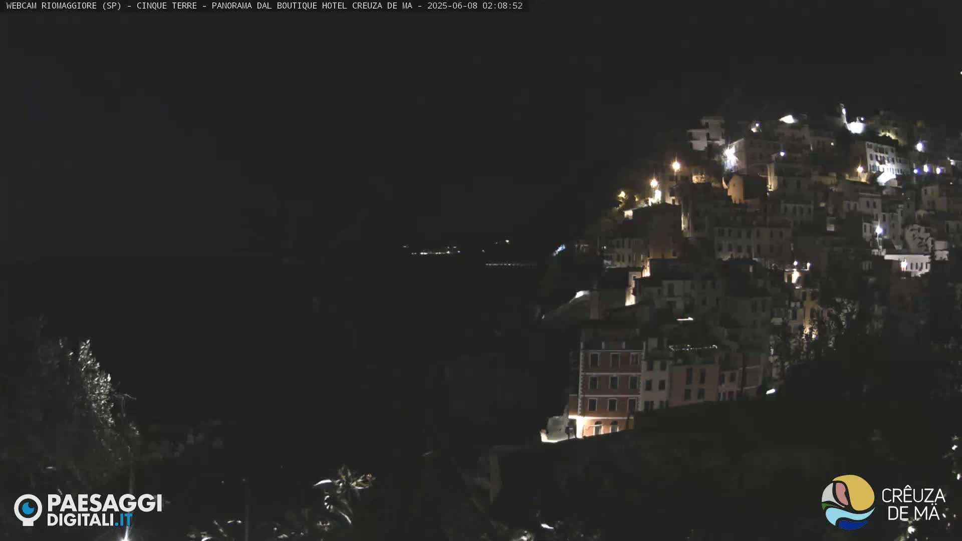 A nighttime view of a hillside town with many lights illuminated, overlooking a dark body of water.