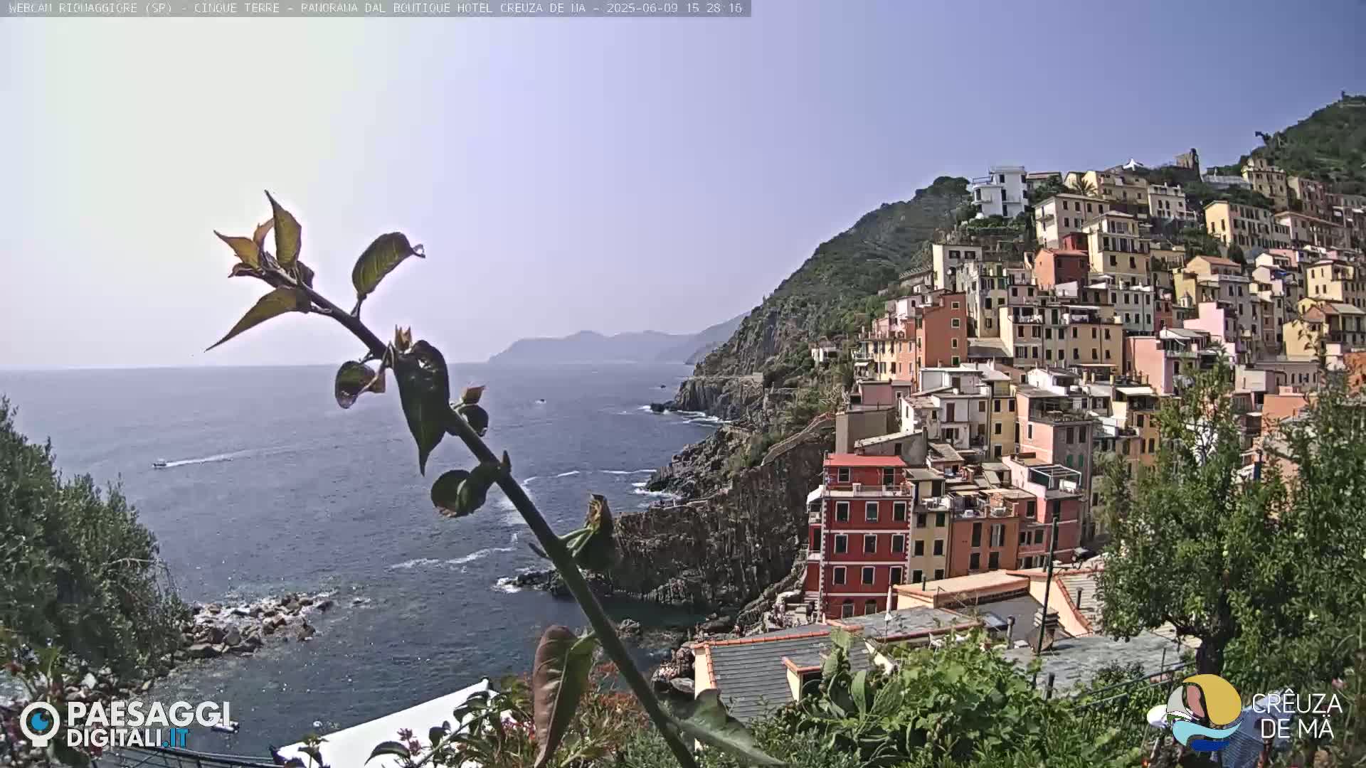 A coastal town with colorful buildings on a hillside overlooking a calm blue sea under a clear sky.