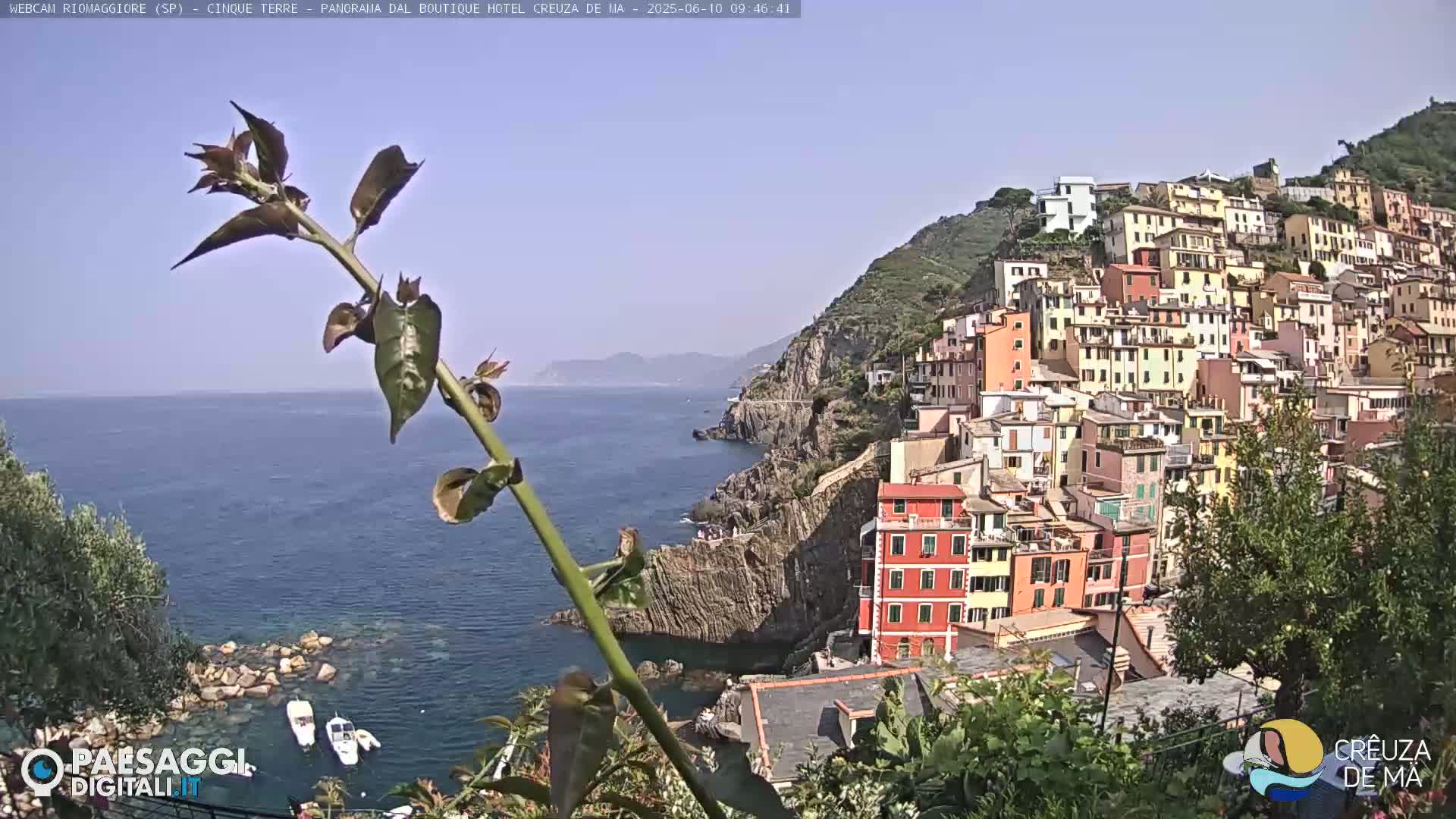 A coastal village of colorful buildings clinging to a hillside, overlooks a calm blue sea on a sunny day.