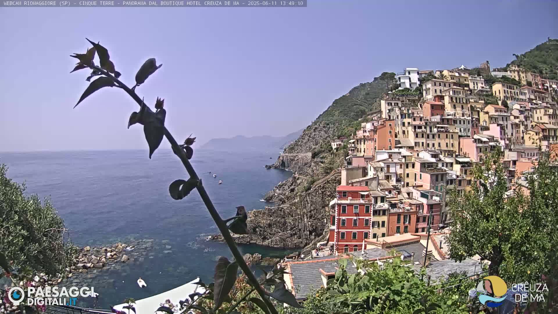 A coastal village of colorful buildings clings to a hillside overlooking a calm blue sea on a clear, sunny day.