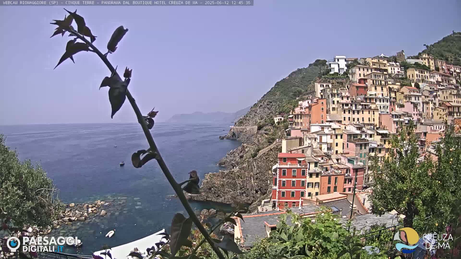 A coastal village with colorful buildings clinging to a hillside overlooks a calm blue sea under a clear sky.