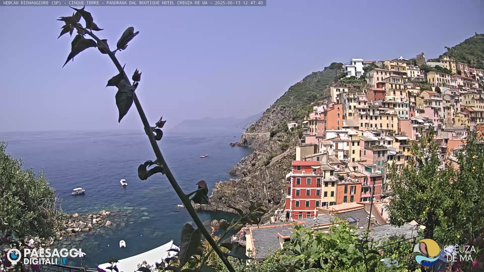 A hillside village of colorful buildings overlooks a calm blue sea on a clear, sunny day.