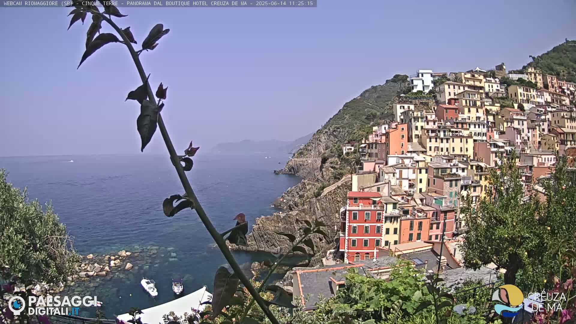 A coastal town of colorful buildings clings to a hillside overlooking a calm, blue sea under a clear sky.