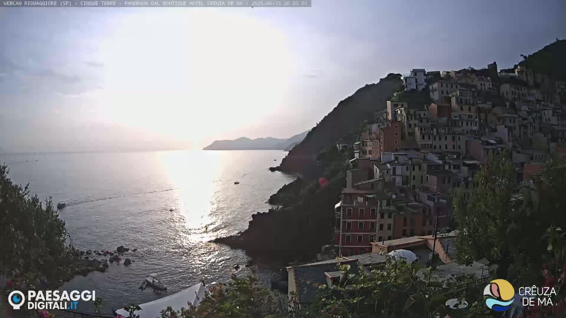 A coastal town built on a steep hillside overlooks a calm sea under a mostly clear sky.