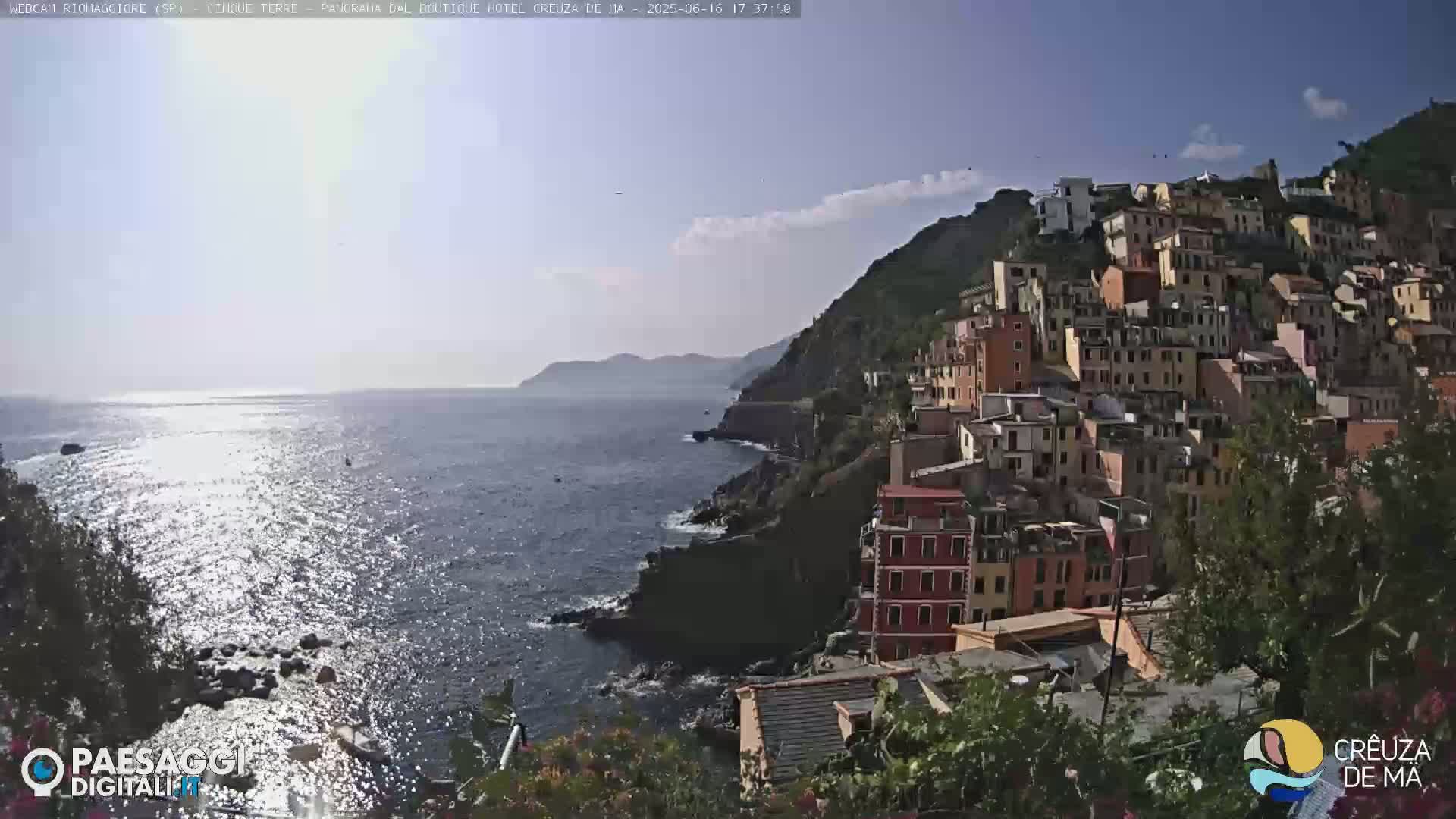 A coastal town with colorful buildings clings to a hillside overlooking a sparkling blue sea under a mostly clear sky.