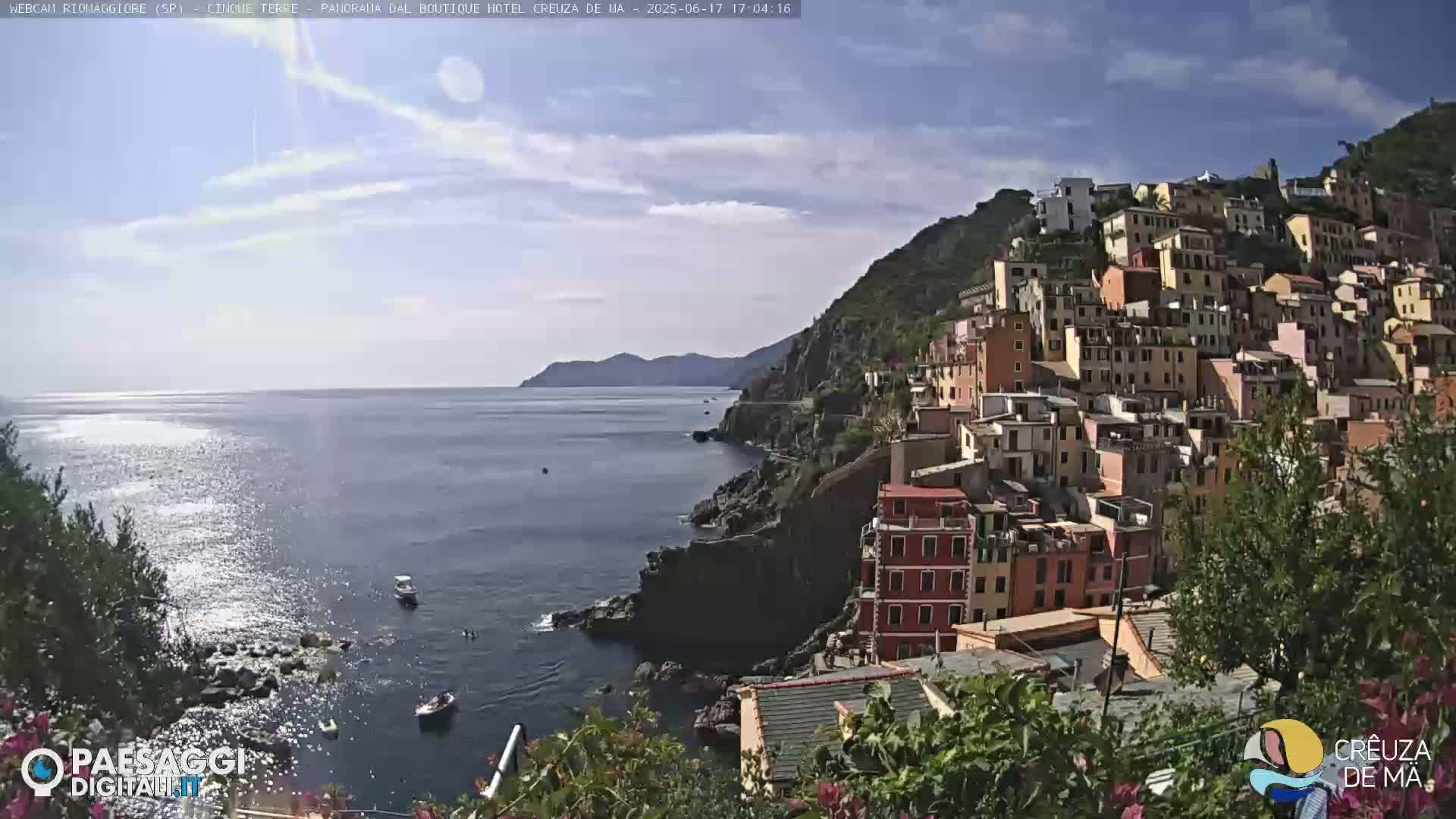 A colorful hillside town clings to a steep cliff overlooking a calm, sunlit sea.