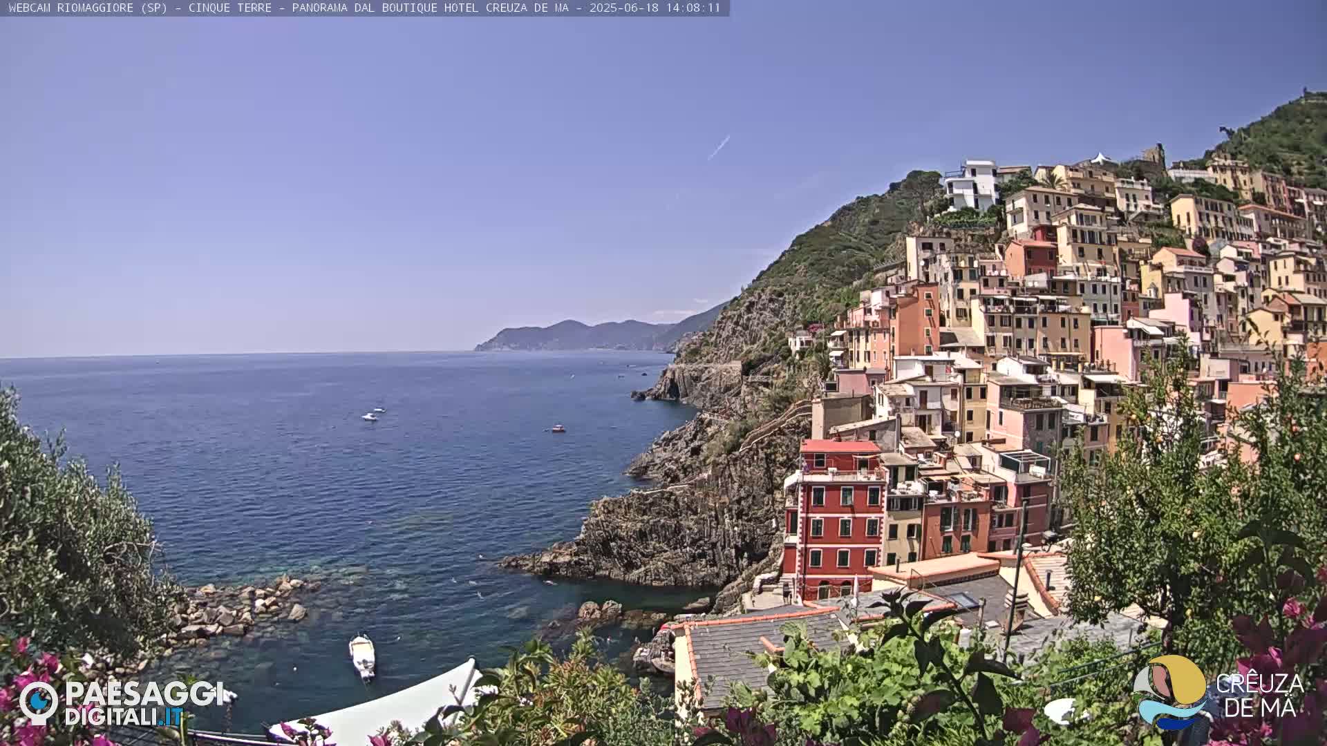 A colorful village clings to a steep hillside overlooking a calm blue sea on a sunny day.