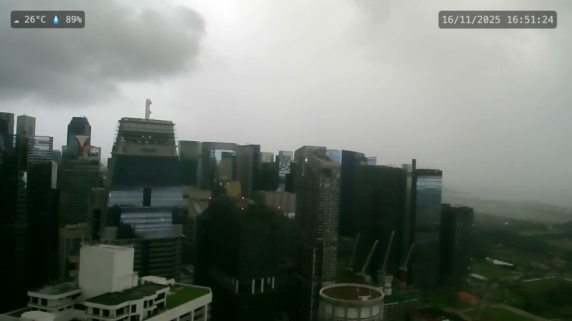 An expansive cityscape featuring numerous modern skyscrapers is visible under a heavily overcast, gray, and hazy sky, suggesting damp weather conditions.