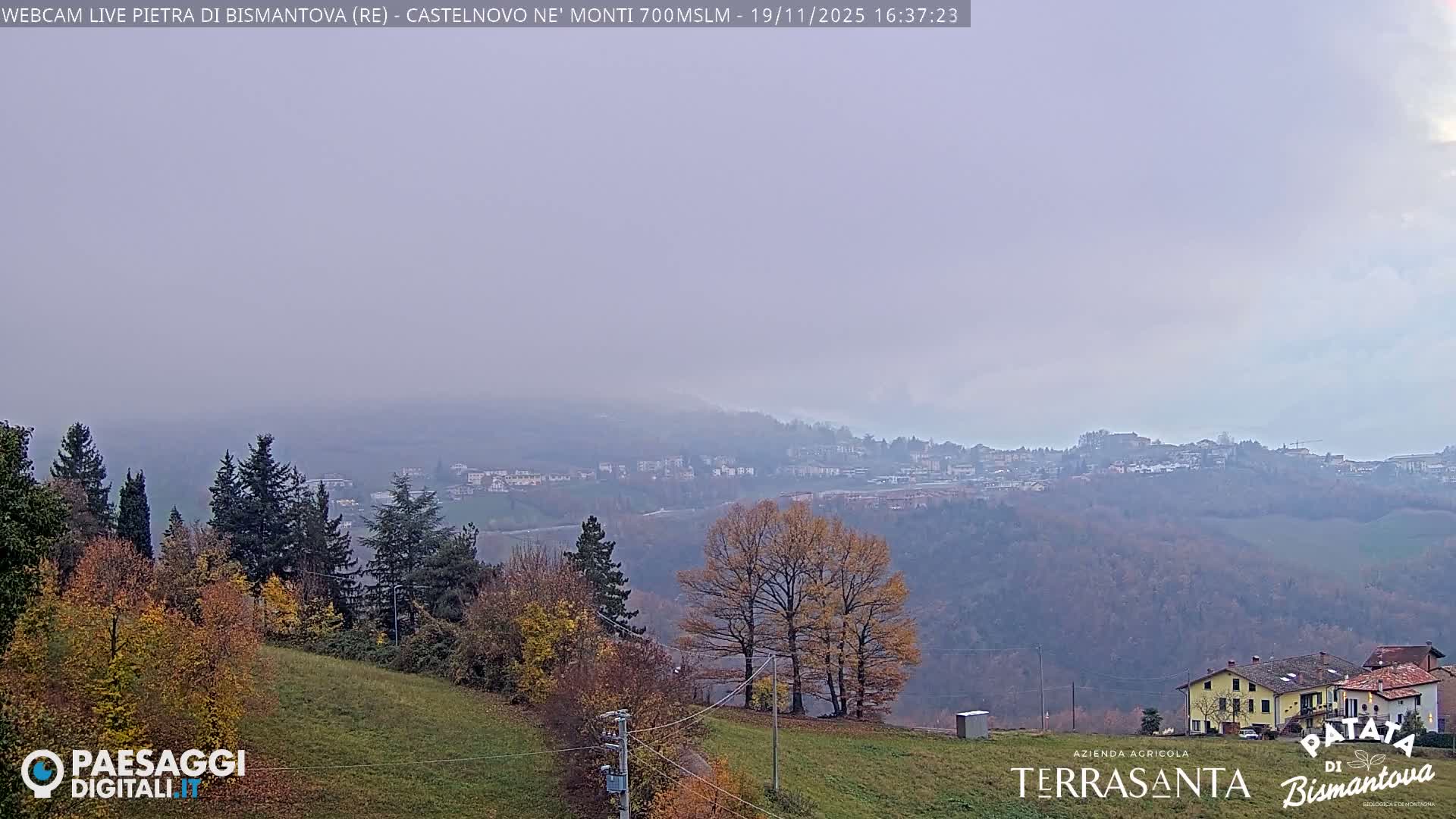 An overcast day reveals a broad landscape with a prominent flat-topped mountain, a village nestled among rolling hills displaying rich autumn foliage, and scattered houses in the foreground.