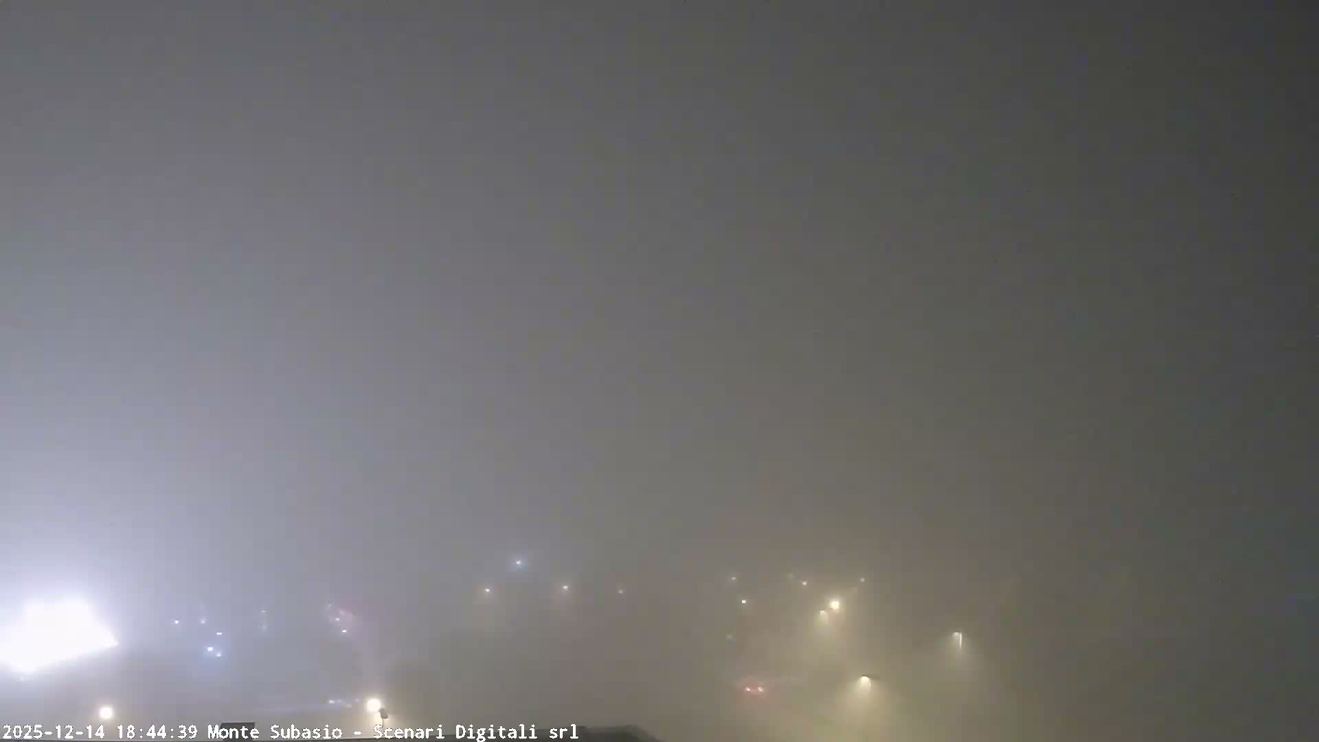 An expansive outdoor view reveals a town featuring red-roofed buildings, roads, and a large solar panel array amidst autumnal trees, set against a backdrop of rolling hills and a prominent mountain under a bright, partly cloudy sky.