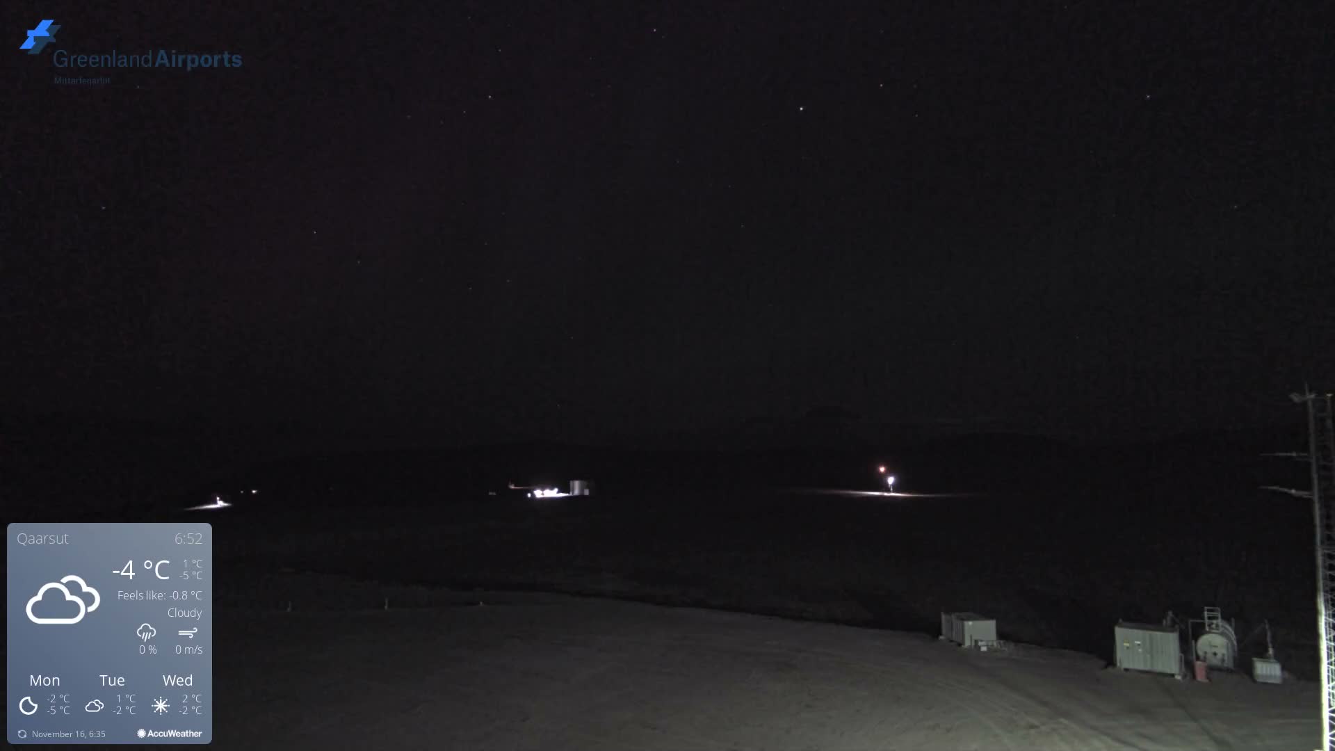 A very dark outdoor nighttime view of an airport area features faint distant lights and foreground structures under a mostly clear sky with scattered stars.