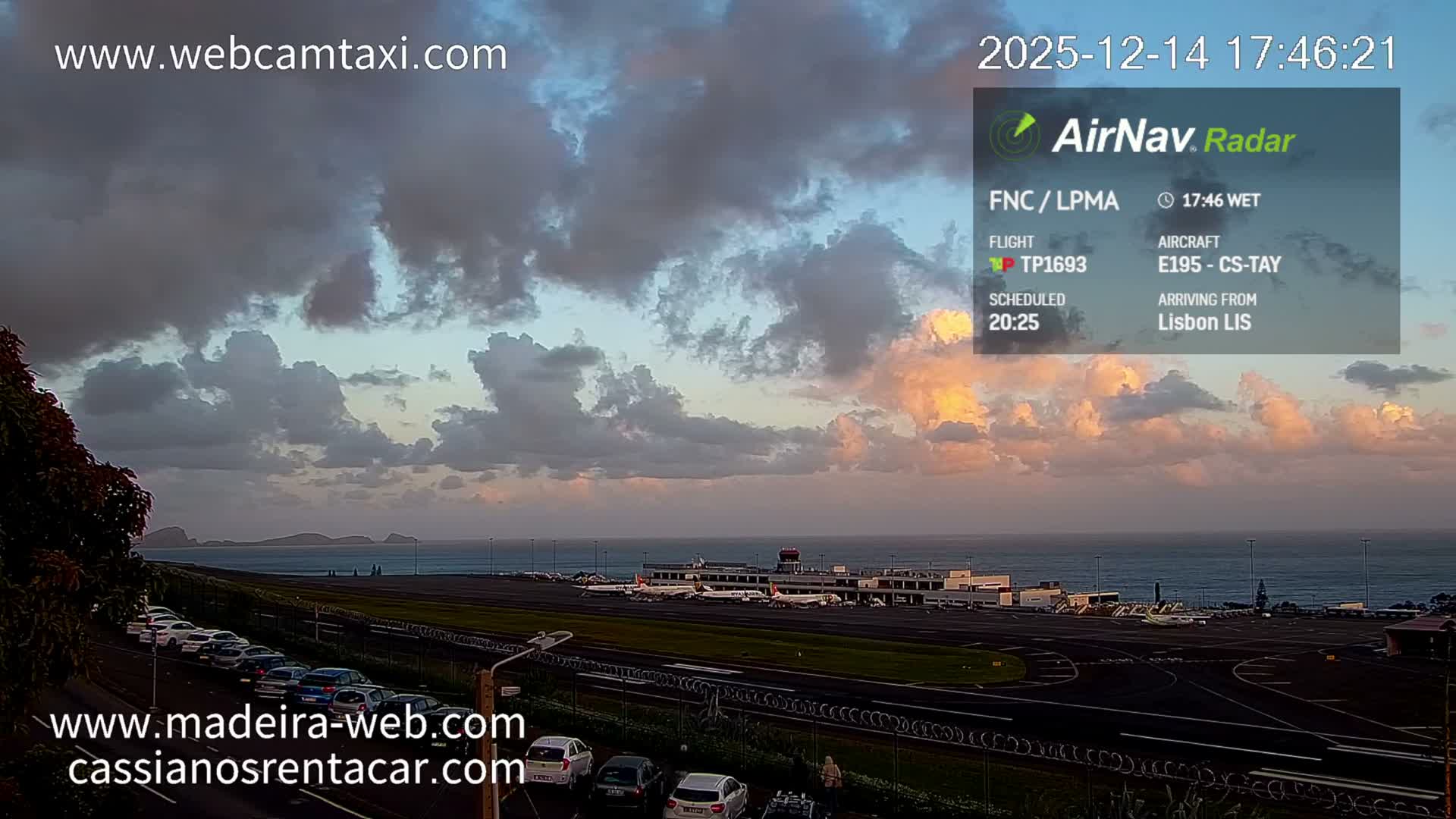 A bright and sunny morning with scattered clouds overlooks a shimmering sea reflecting the sun's glare, a distant coastline, and some foreground buildings.