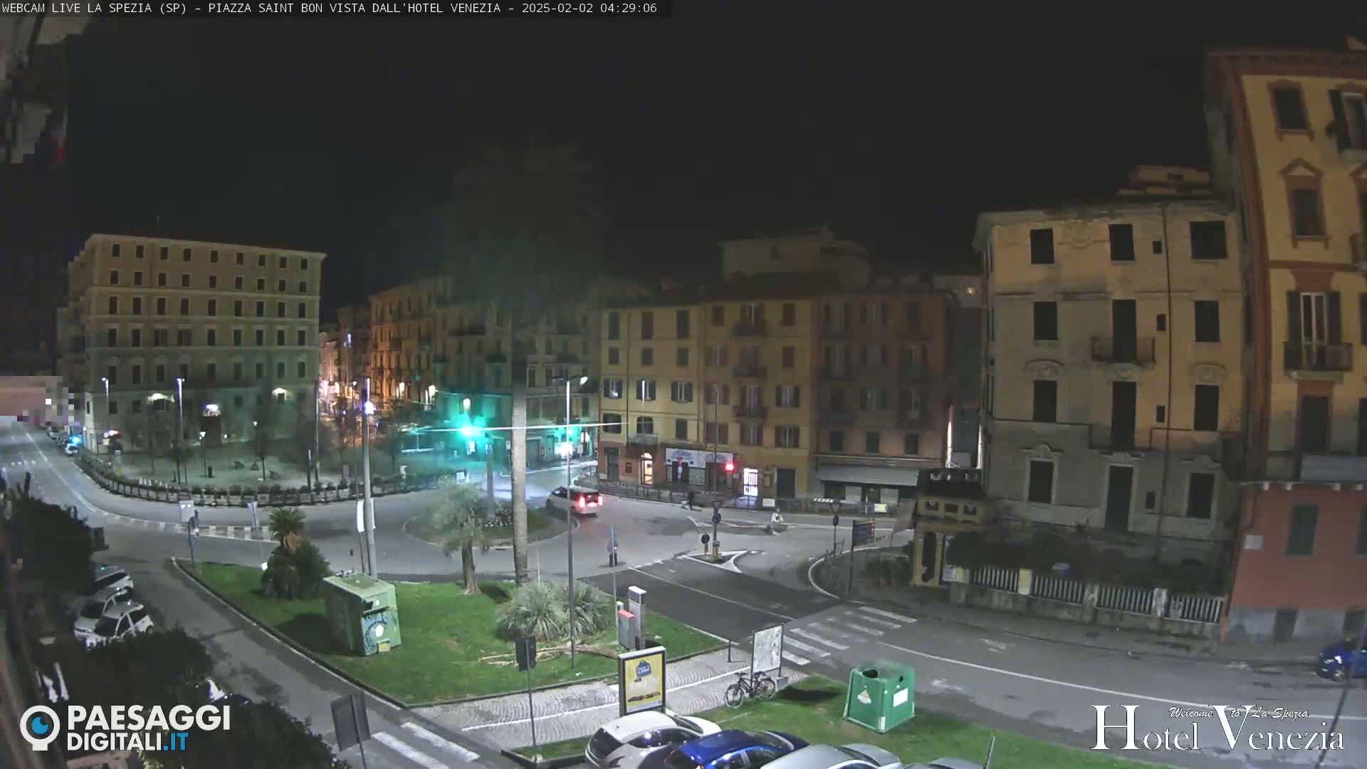 A nighttime view of a mostly empty town square with several multi-story buildings surrounding it.