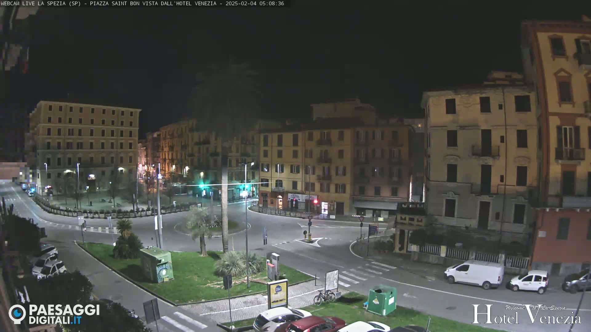 A nighttime view of a mostly empty, circular plaza surrounded by multi-story buildings.
