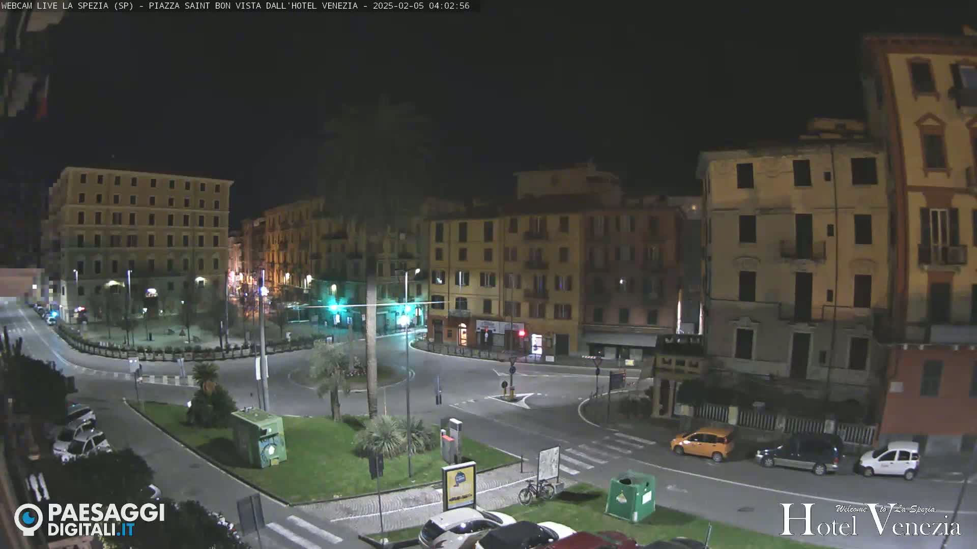 A nighttime view of a city square with several multi-story buildings surrounding it, and a few cars parked along the sides.