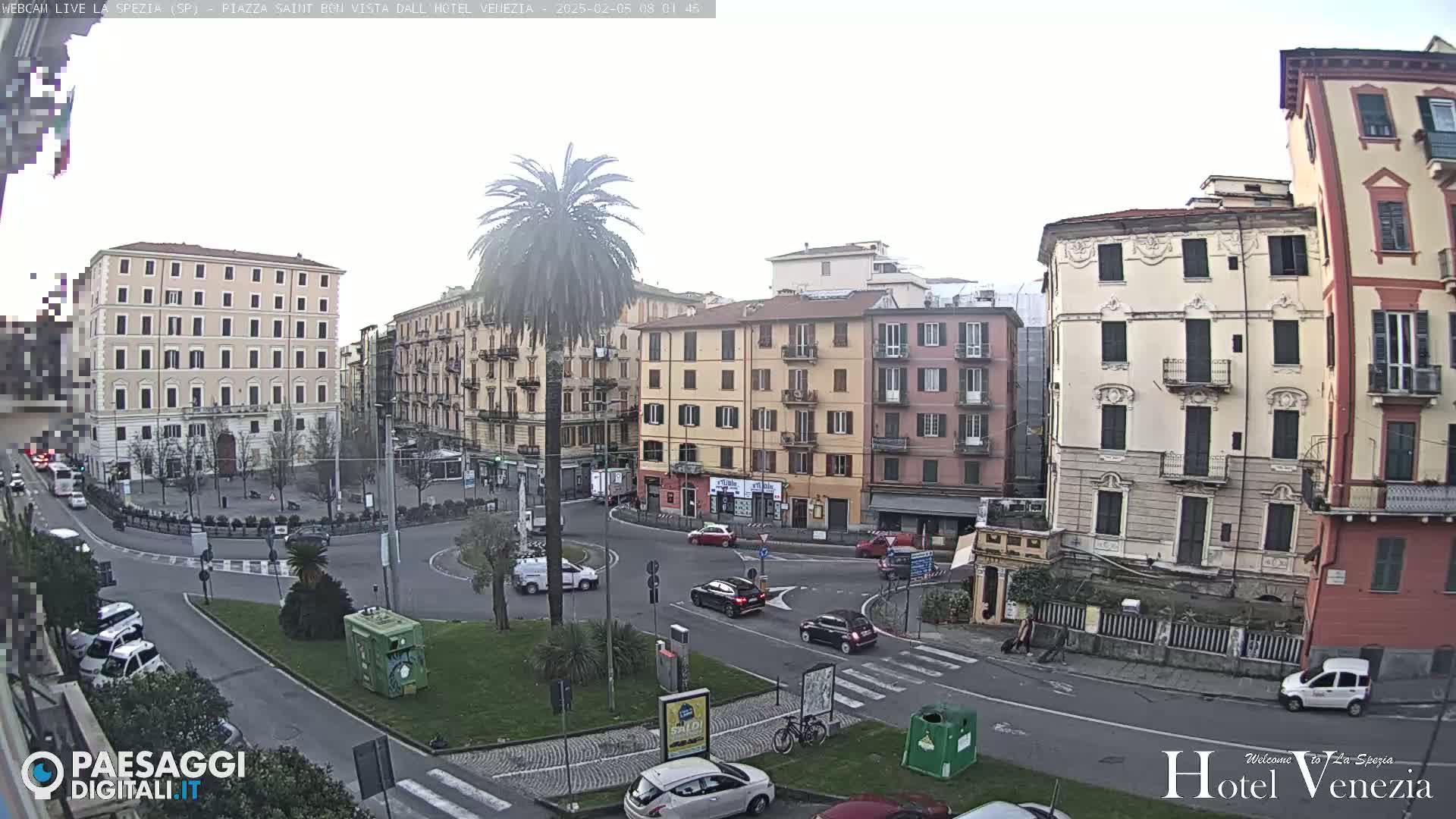 A mostly cloudy day reveals a circular traffic intersection surrounded by multi-story buildings in a European city, with several cars visible.