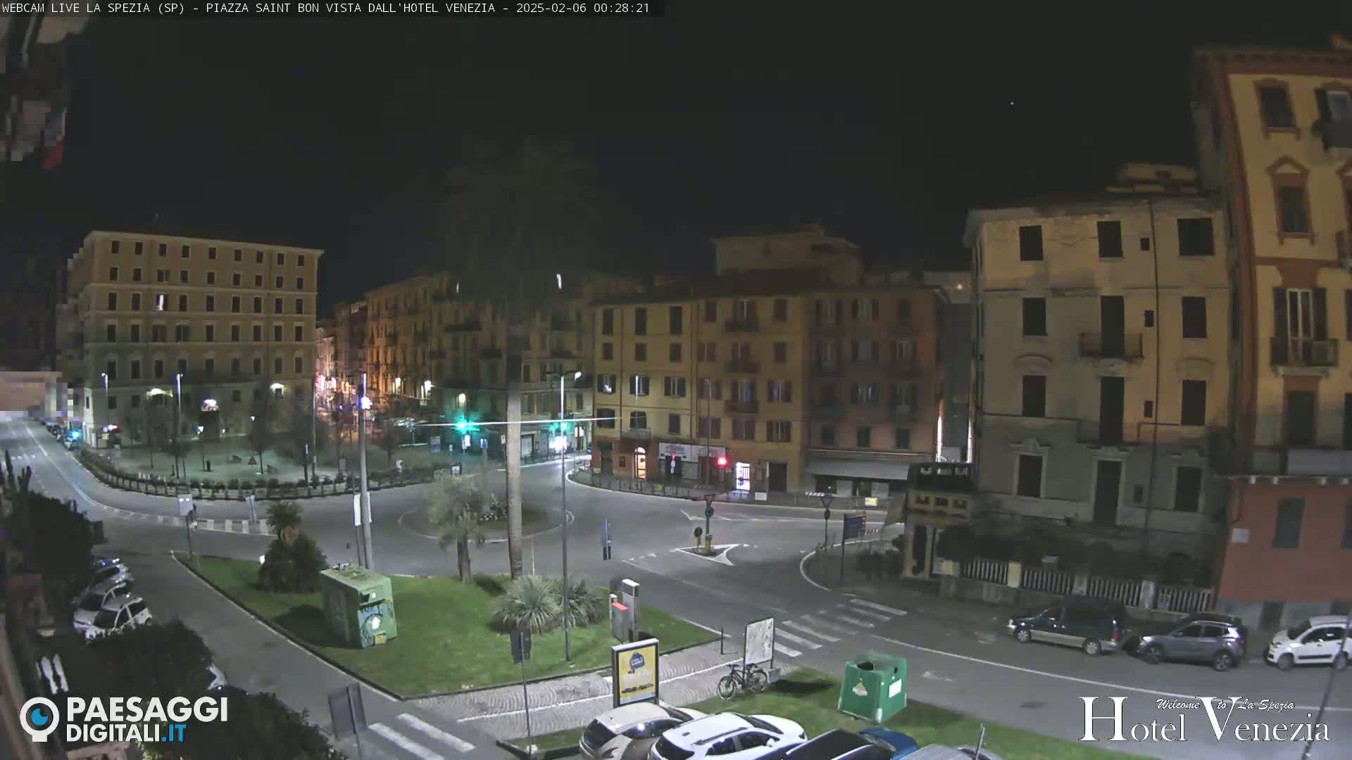 A nighttime view of a mostly empty town square surrounded by multi-story buildings under a clear, dark sky.
