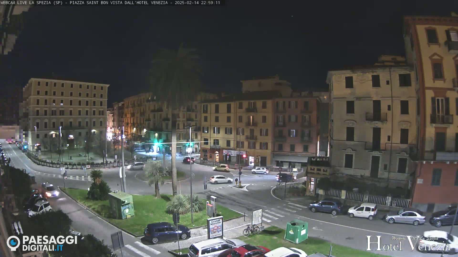 A nighttime, aerial view of a European town square with several cars and buildings illuminated under a clear sky.