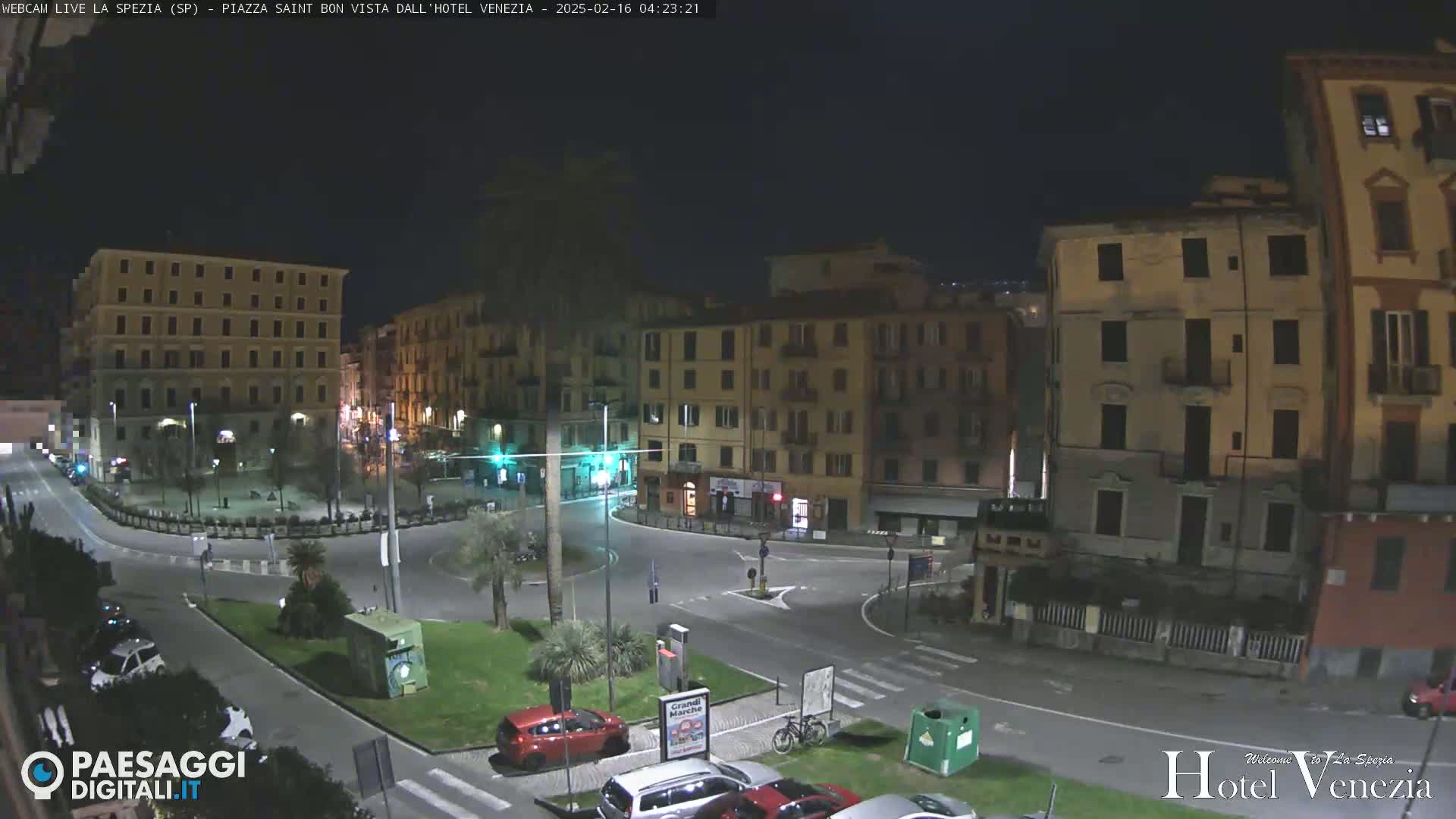 A nighttime view of a mostly empty town square surrounded by multi-story buildings under a dark sky.