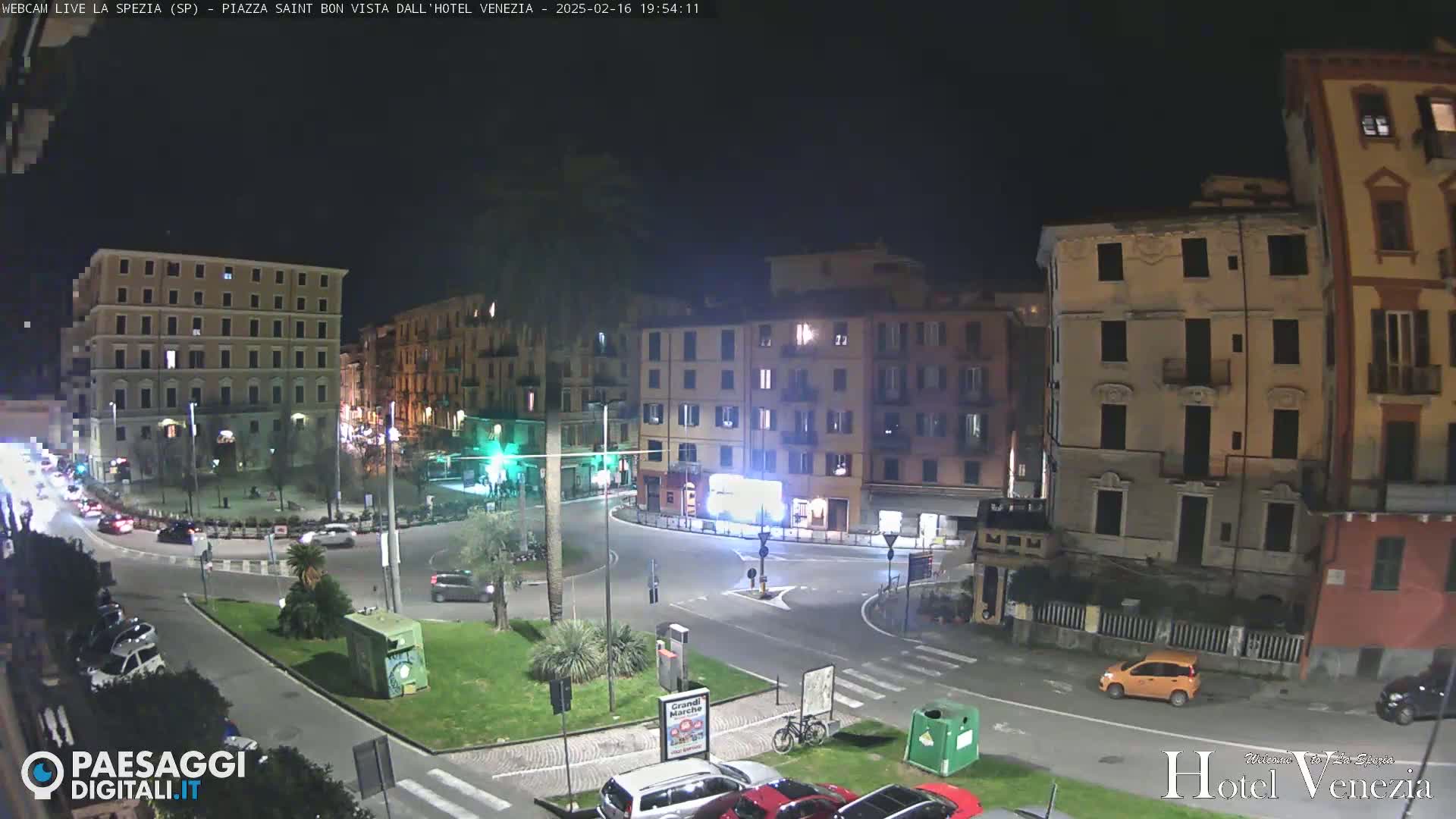 A nighttime view of a traffic circle in a city, surrounded by multi-story buildings.