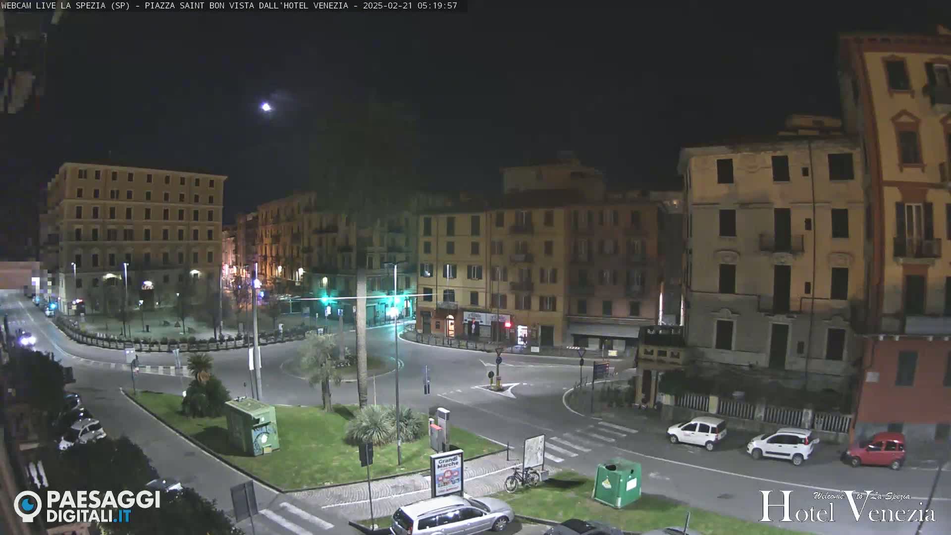 A nighttime view of a mostly empty town square with several buildings surrounding it, under a clear sky.