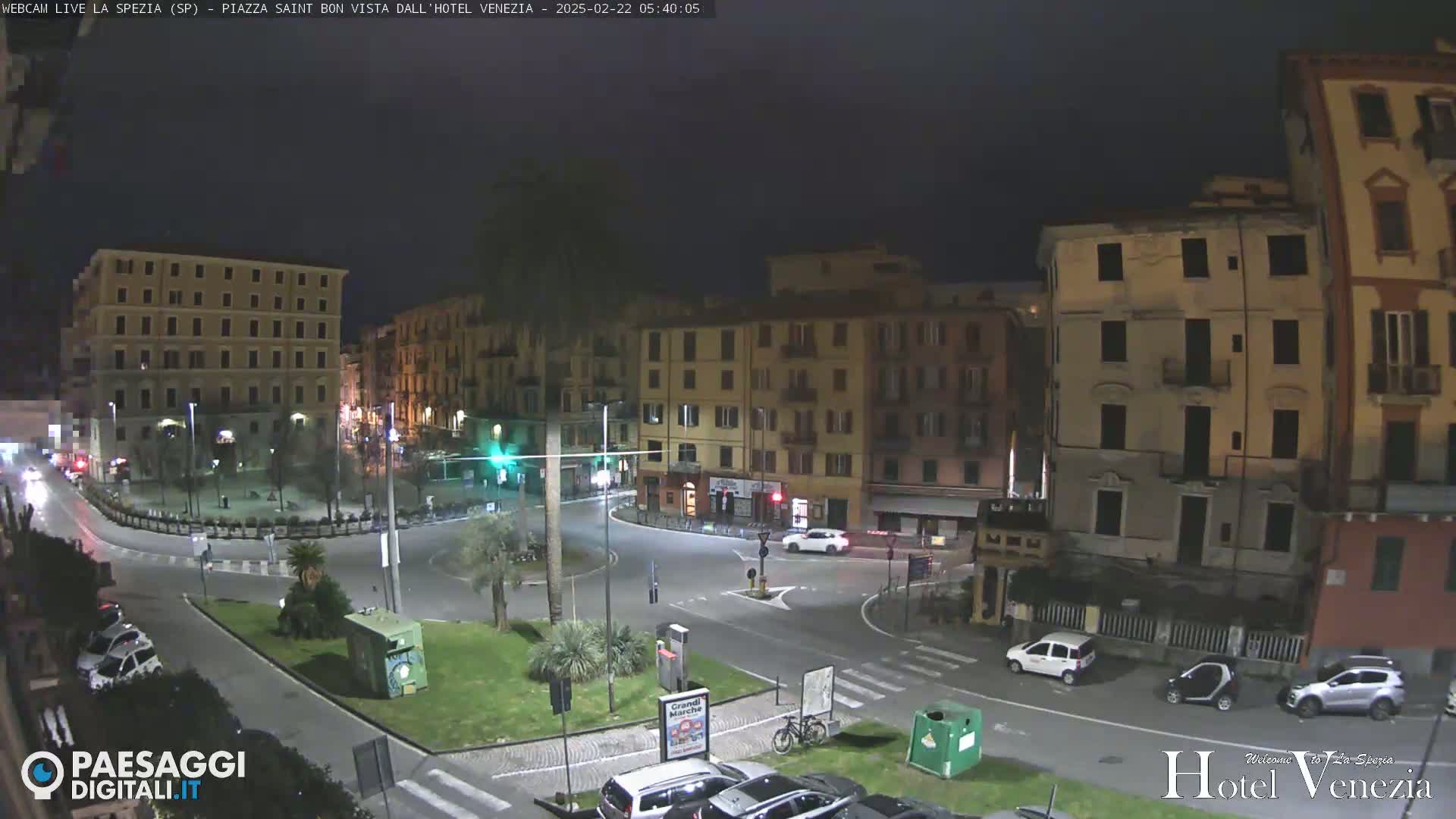 A nighttime view of a mostly empty town square surrounded by multi-story buildings.