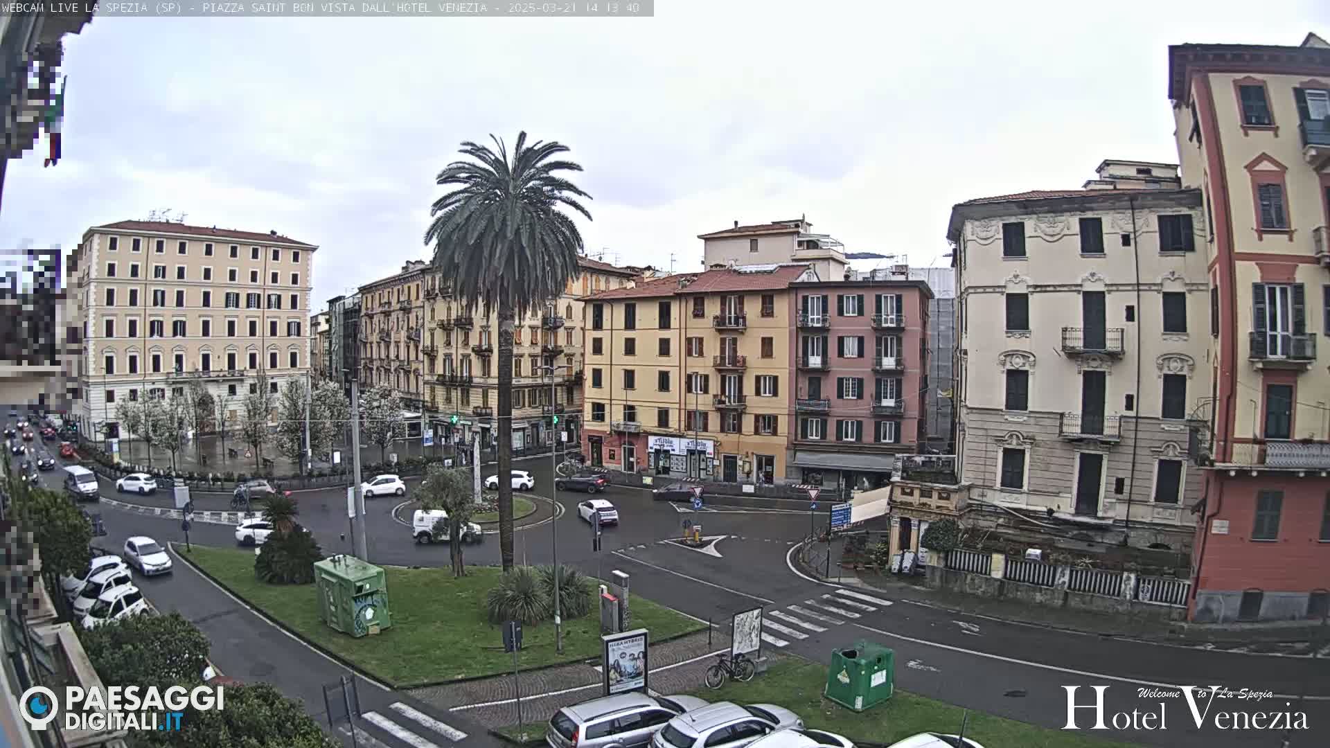 A city square with several multi-story buildings surrounding a roundabout with light traffic under an overcast sky.