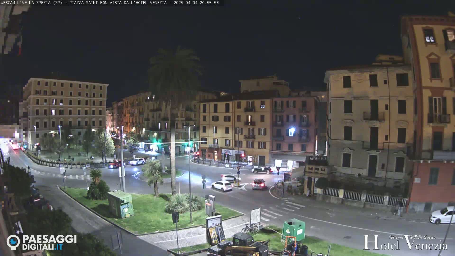 A nighttime view of a traffic circle in a European city, surrounded by multi-story buildings under a clear, dark sky.