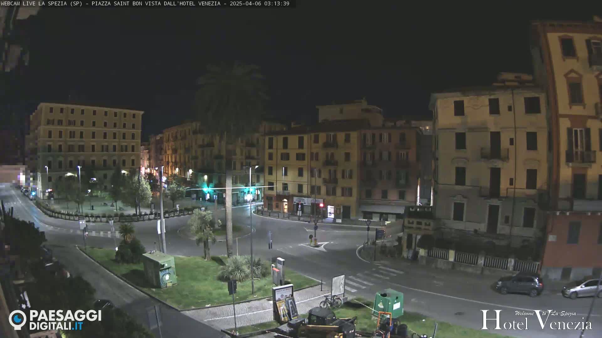 A nighttime view of a city square, illuminated by streetlights, with several multi-story buildings surrounding it.