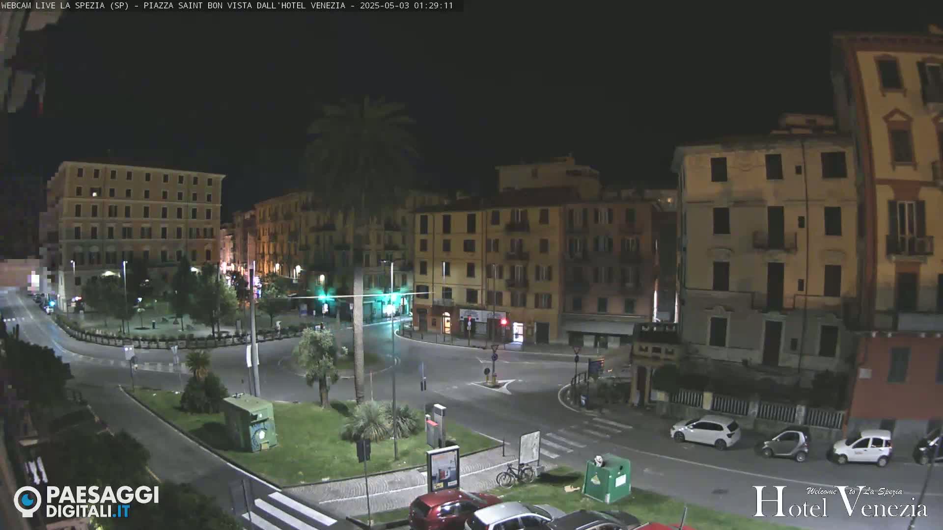 A nighttime, aerial view of a mostly empty town square surrounded by multi-story buildings.