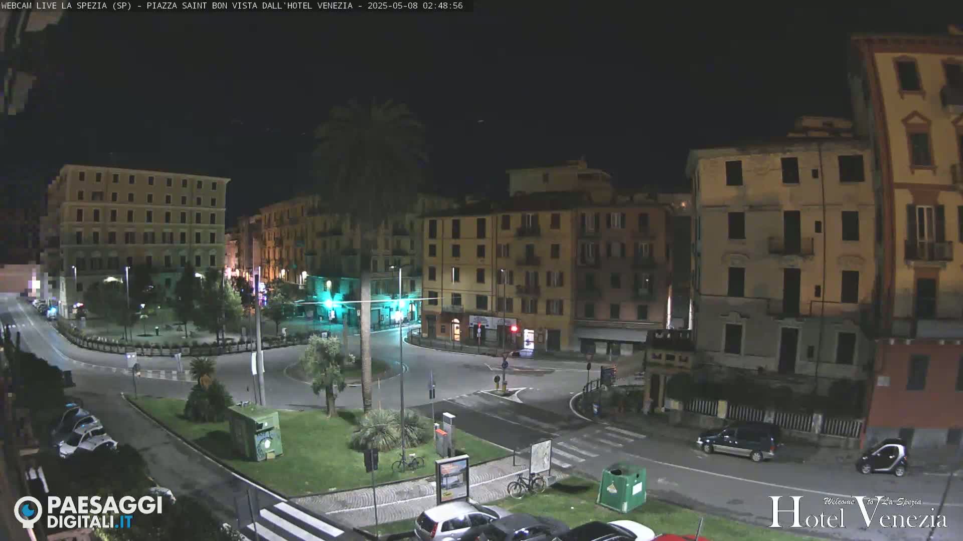A nighttime view of a mostly empty, circular plaza surrounded by multi-story buildings in a city.