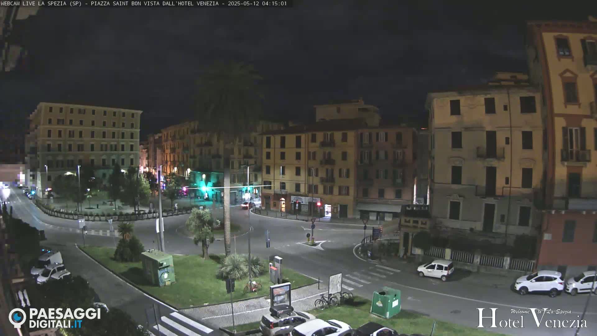A nighttime view of a mostly empty city square surrounded by multi-story buildings under a dark sky.