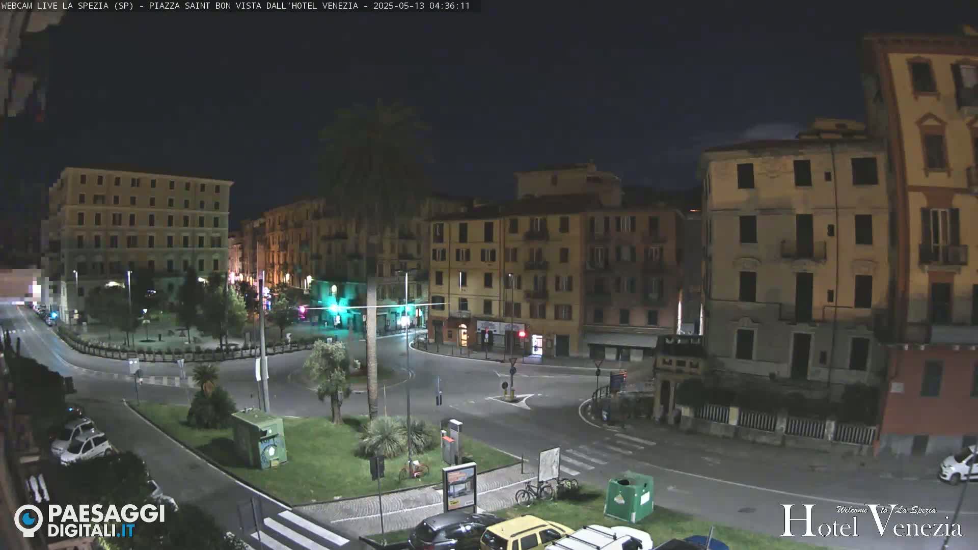 A nighttime view of a mostly empty town square surrounded by multi-story buildings.