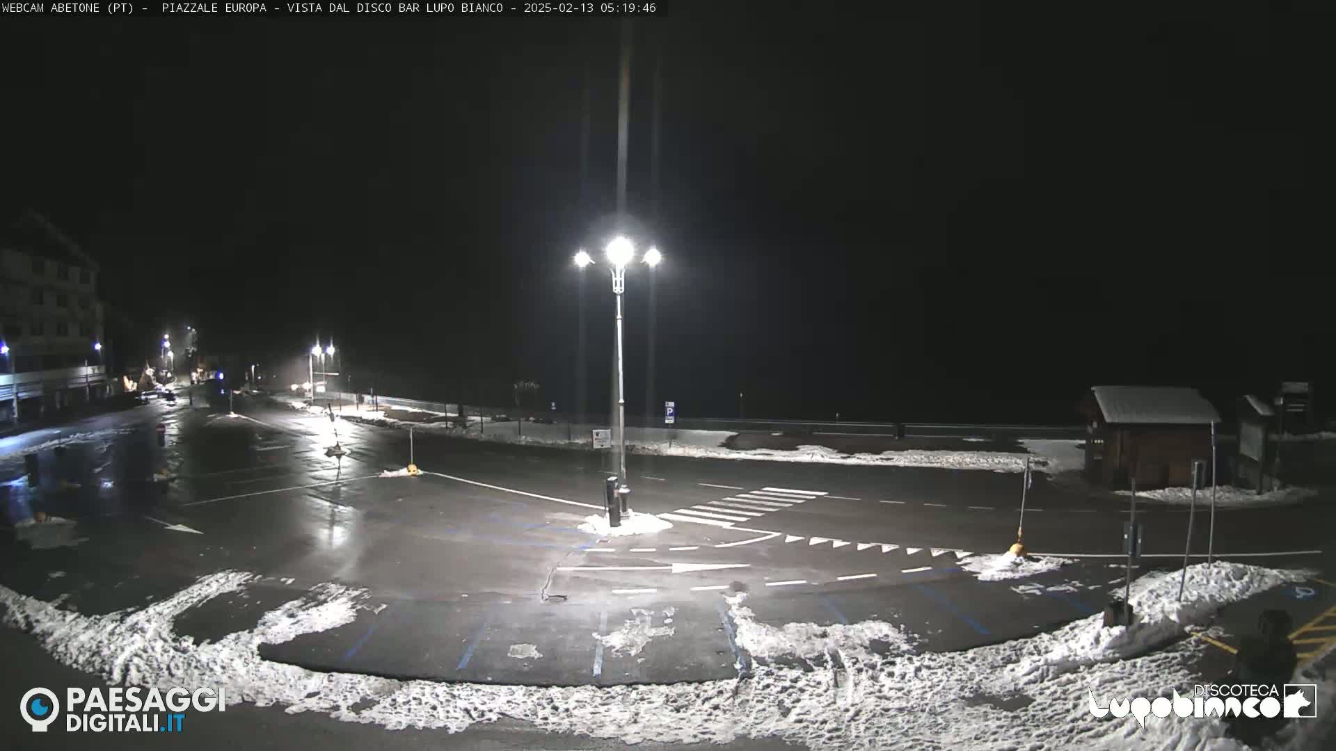 A mostly empty, snow-dusted parking lot at night, illuminated by streetlights.