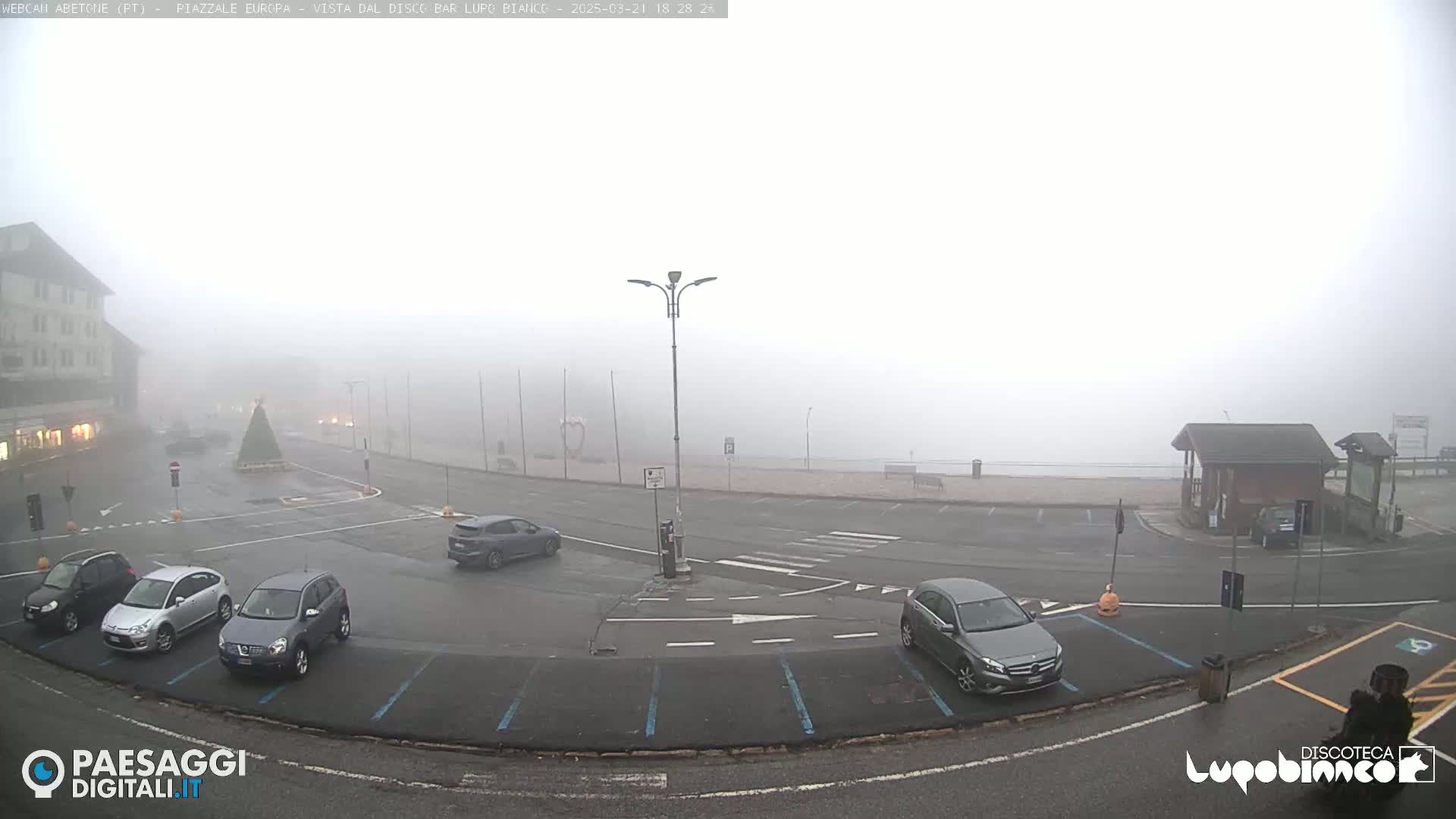 A foggy parking lot with several cars and a building in the background.