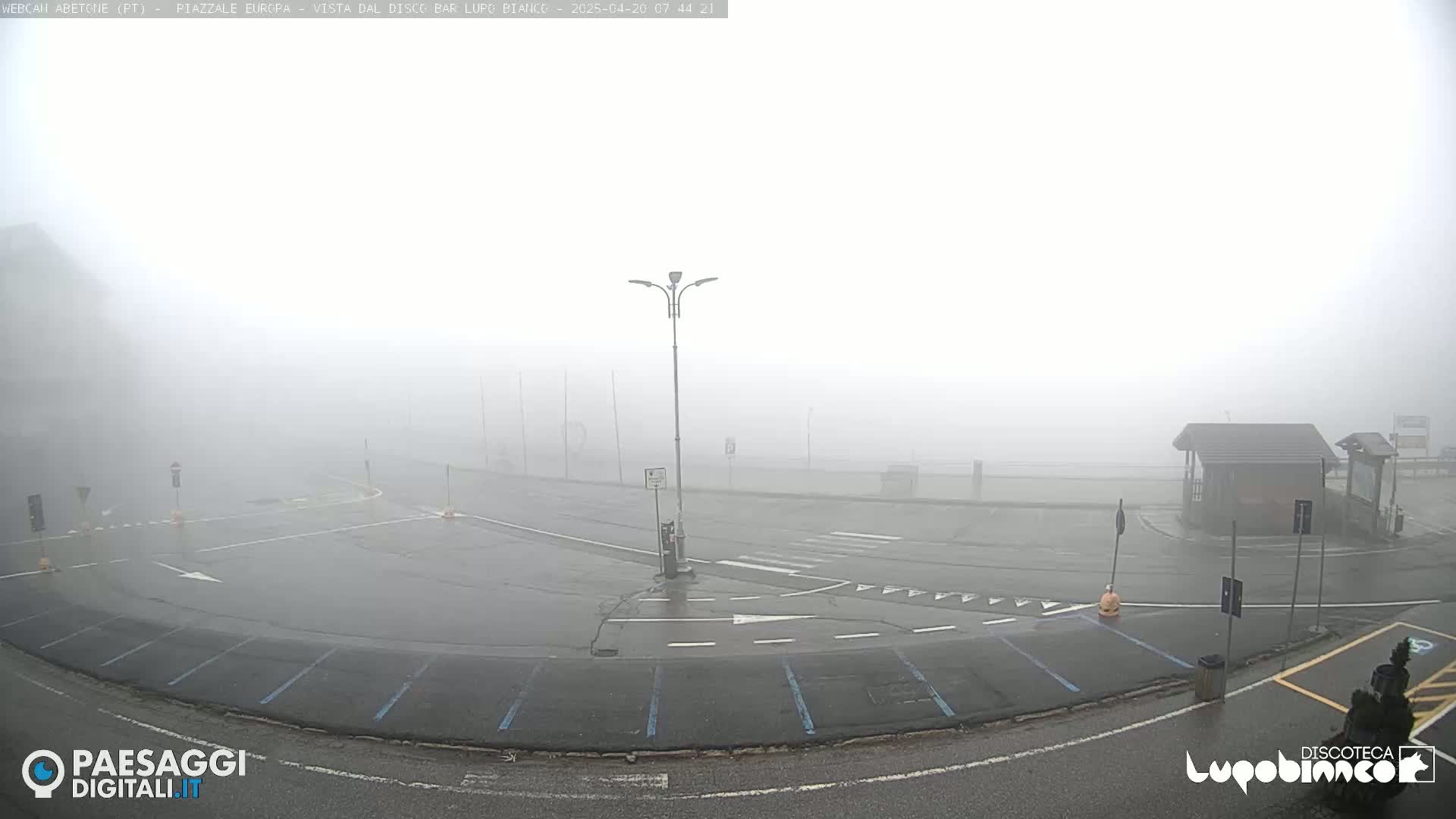 A foggy parking lot with a small building is visible in the distance.