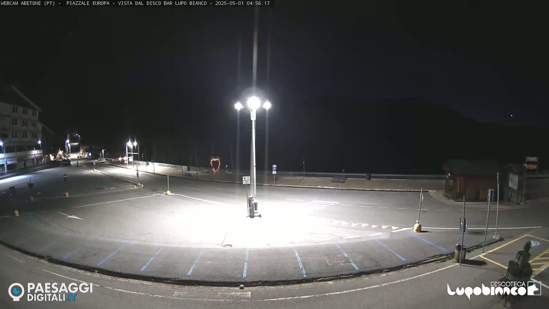 A mostly empty, brightly lit parking lot at night, next to a building, under a dark sky.