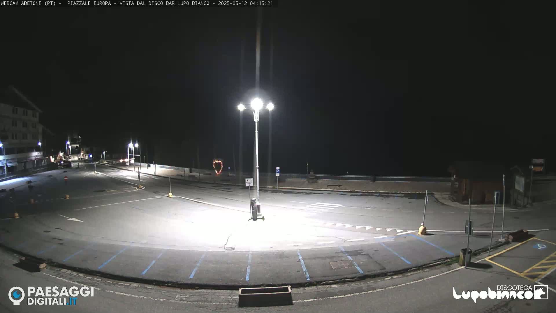 An empty, dark parking lot is illuminated by bright streetlights at night.