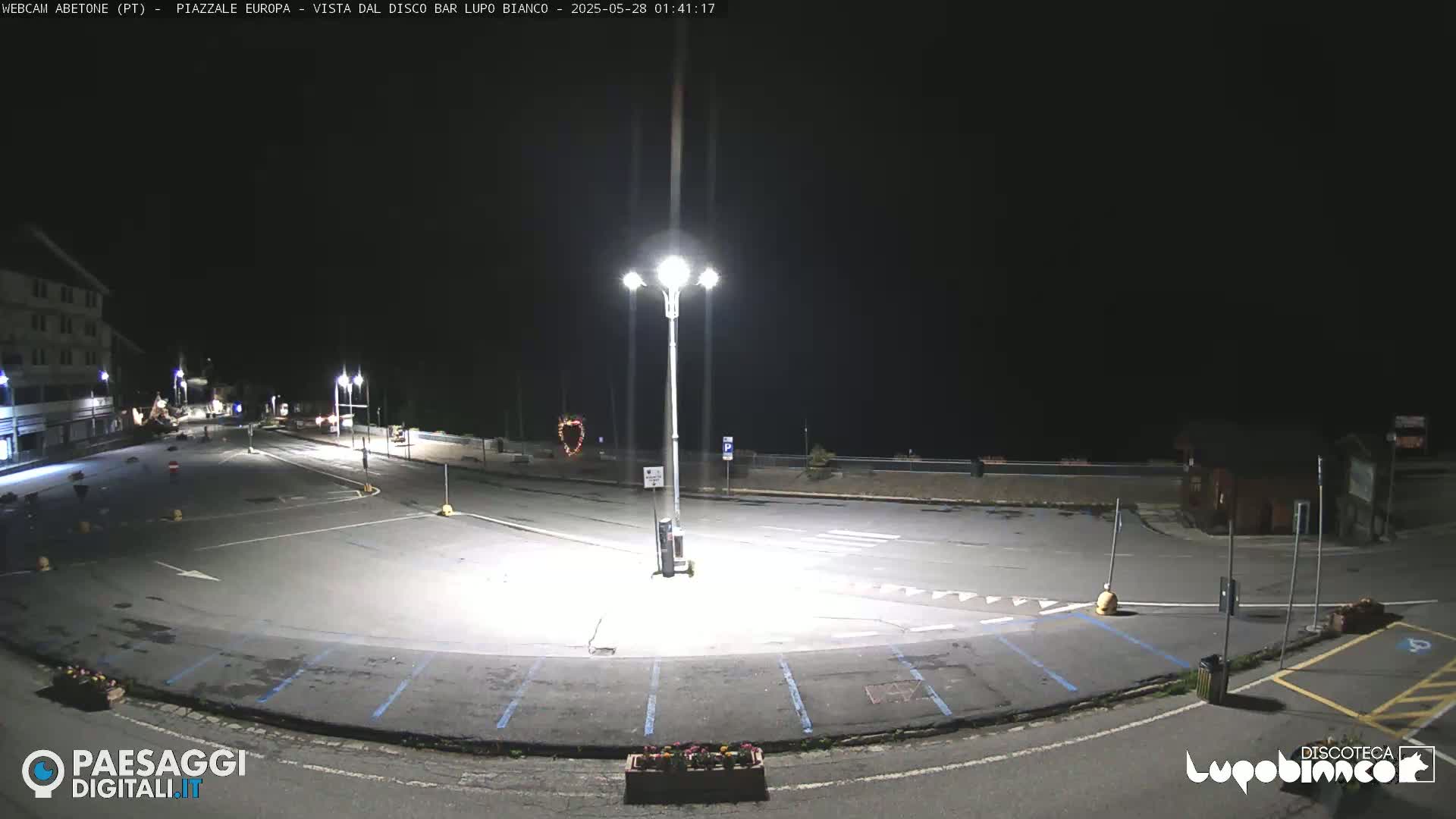 An empty, dark parking lot at night is illuminated by several tall streetlights.