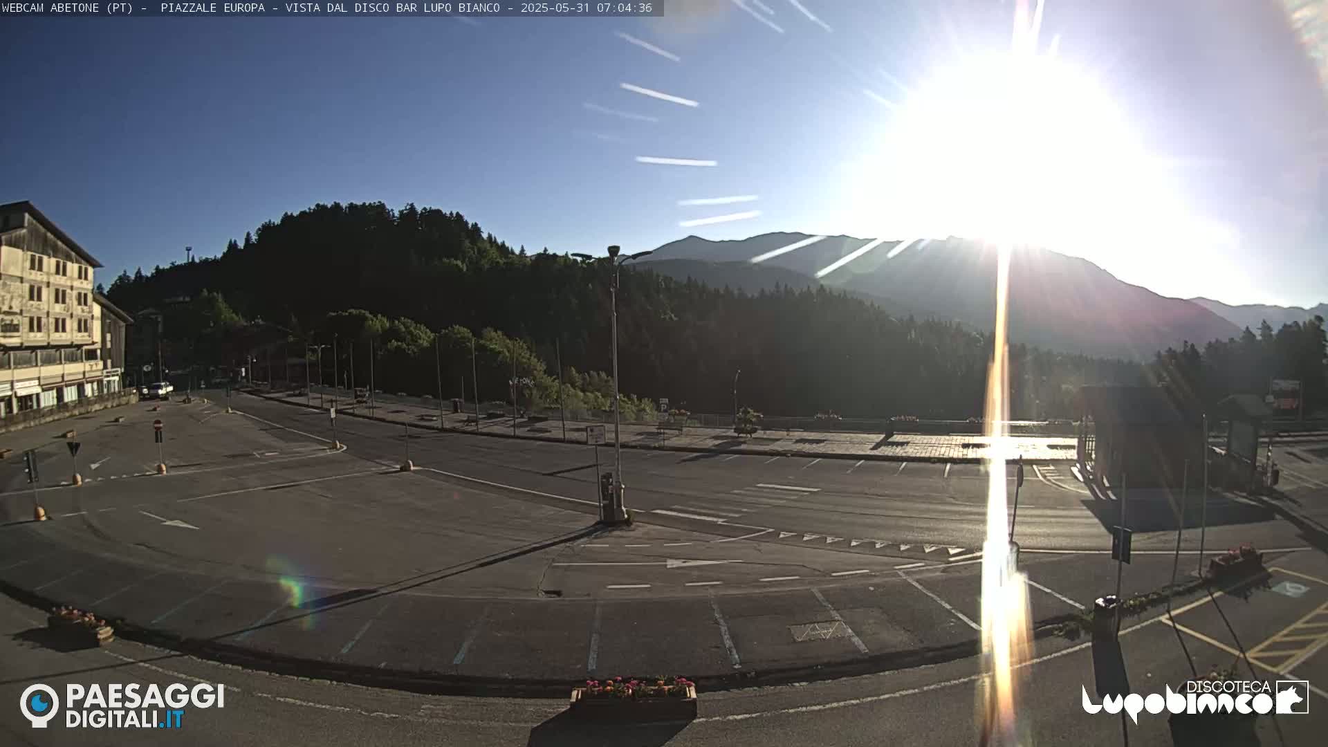 An empty parking lot with a building and mountains in the background on a sunny morning.