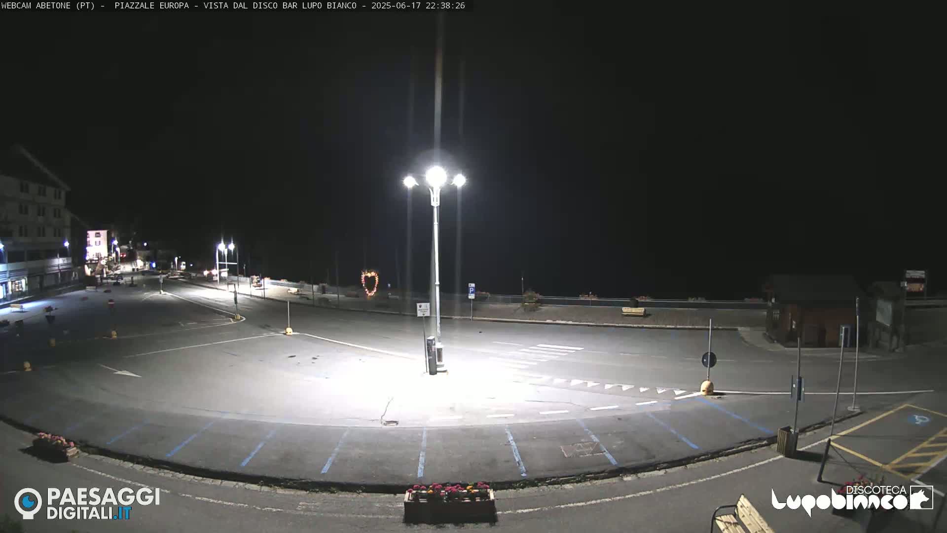 An empty, paved plaza is illuminated by bright streetlights at night.