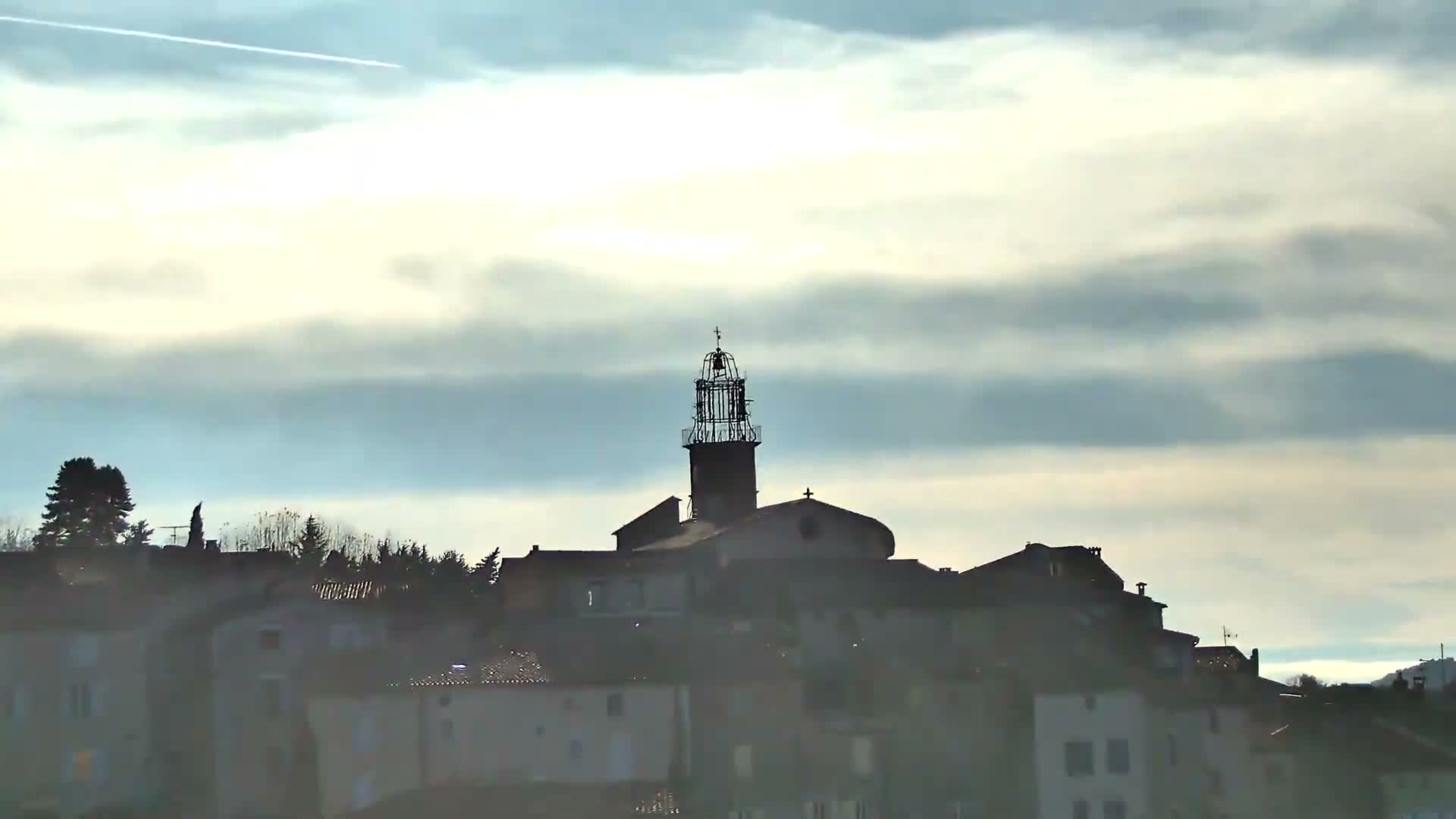 Under a heavily overcast and grey sky, a rural landscape unfolds with rolling hills covered in a mix of green and vibrant autumn foliage, dotted with a few distant houses.