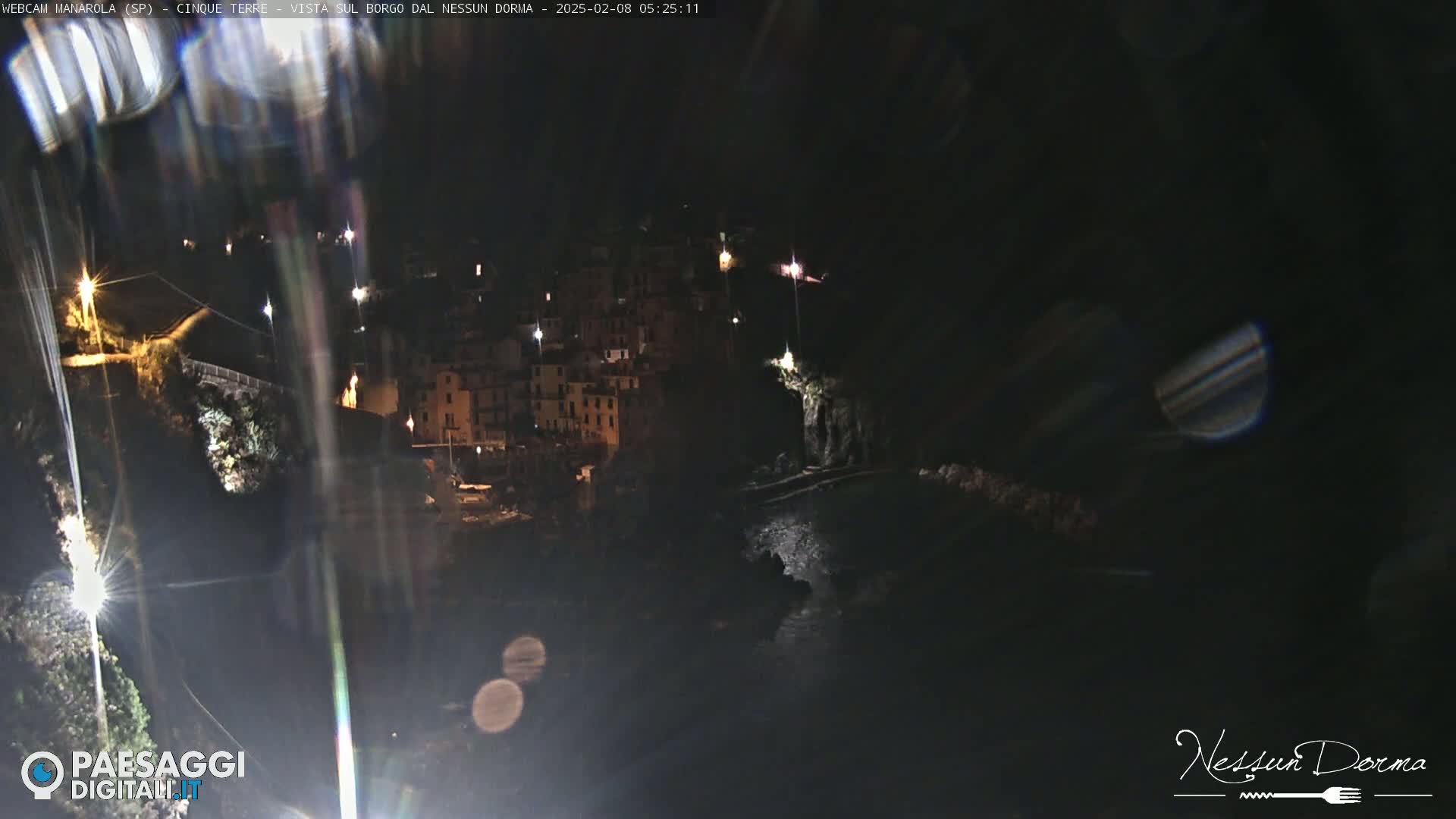 A nighttime, long shot of a coastal town nestled on a cliffside overlooking dark water.