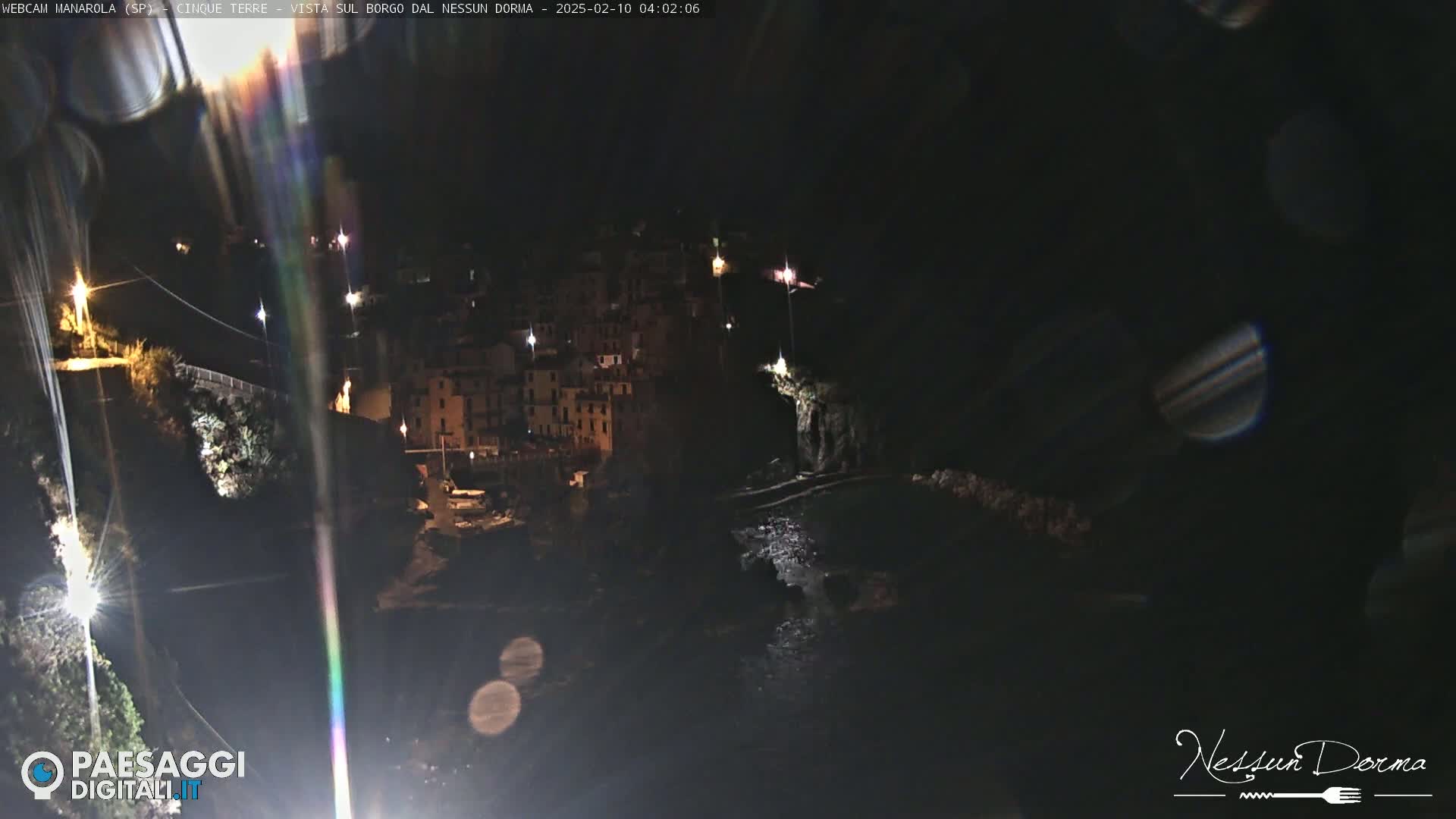 A nighttime view of a coastal town illuminated by streetlights, with a dark, calm body of water below.