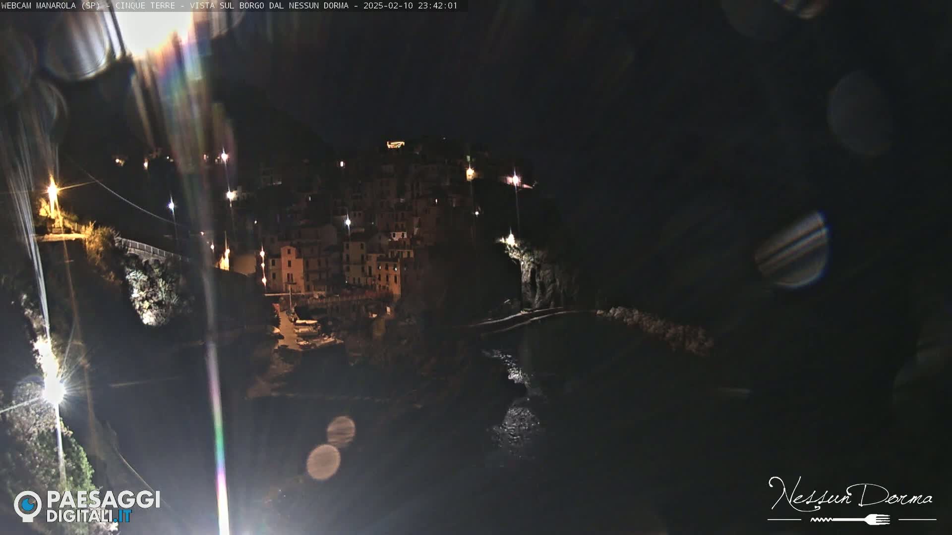 A nighttime view of a coastal town illuminated by lights, nestled between dark cliffs and a body of water.