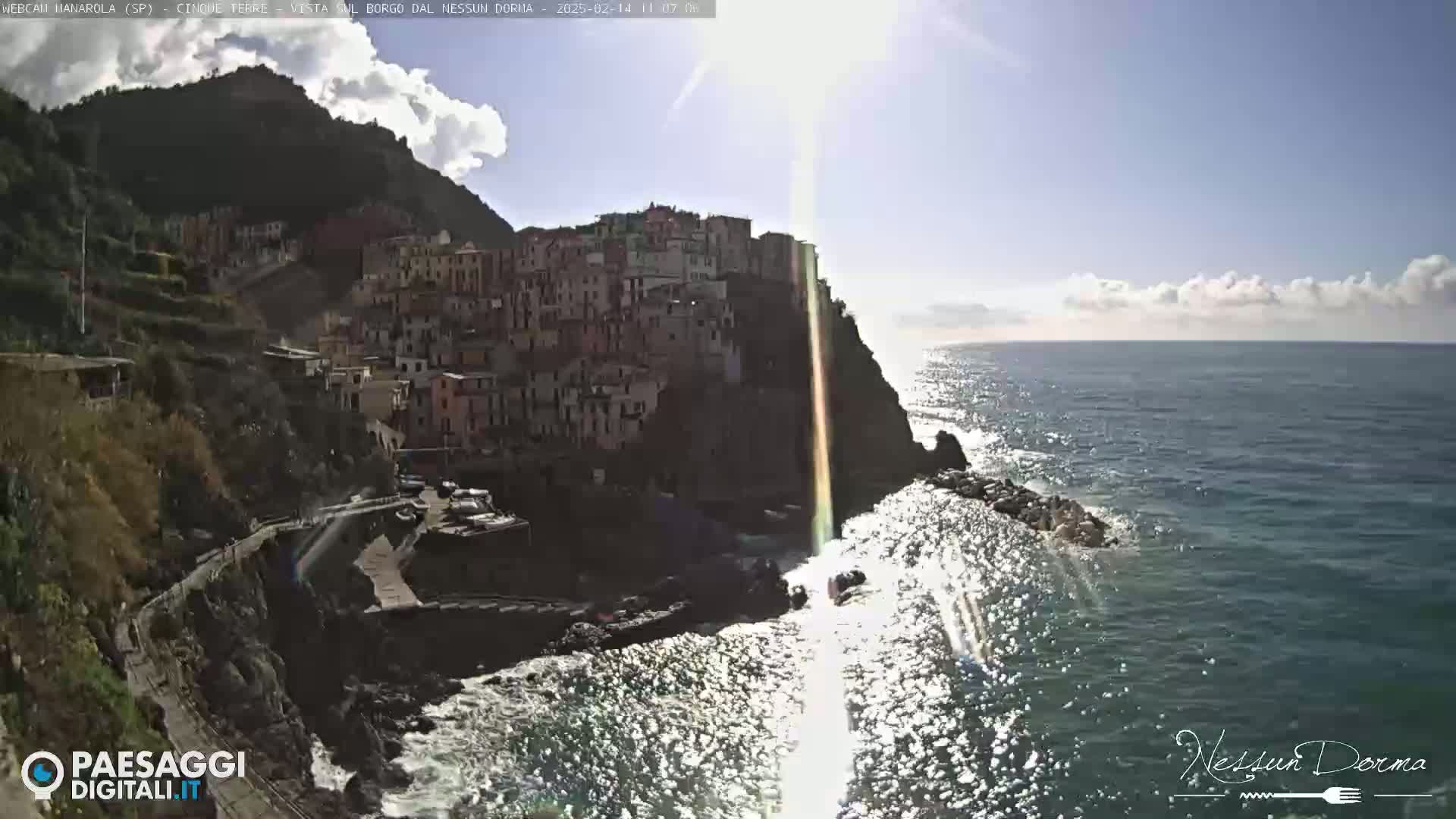 A sunny day overlooking a coastal village built into a cliffside, with a sparkling ocean below.